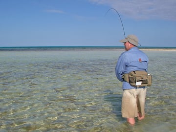 a man standing in shallow water holding a fishing pole