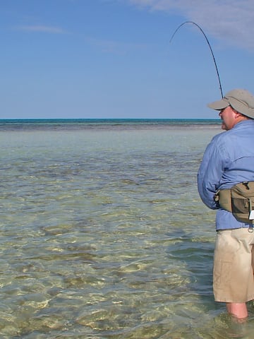 a man standing in shallow water holding a fishing pole