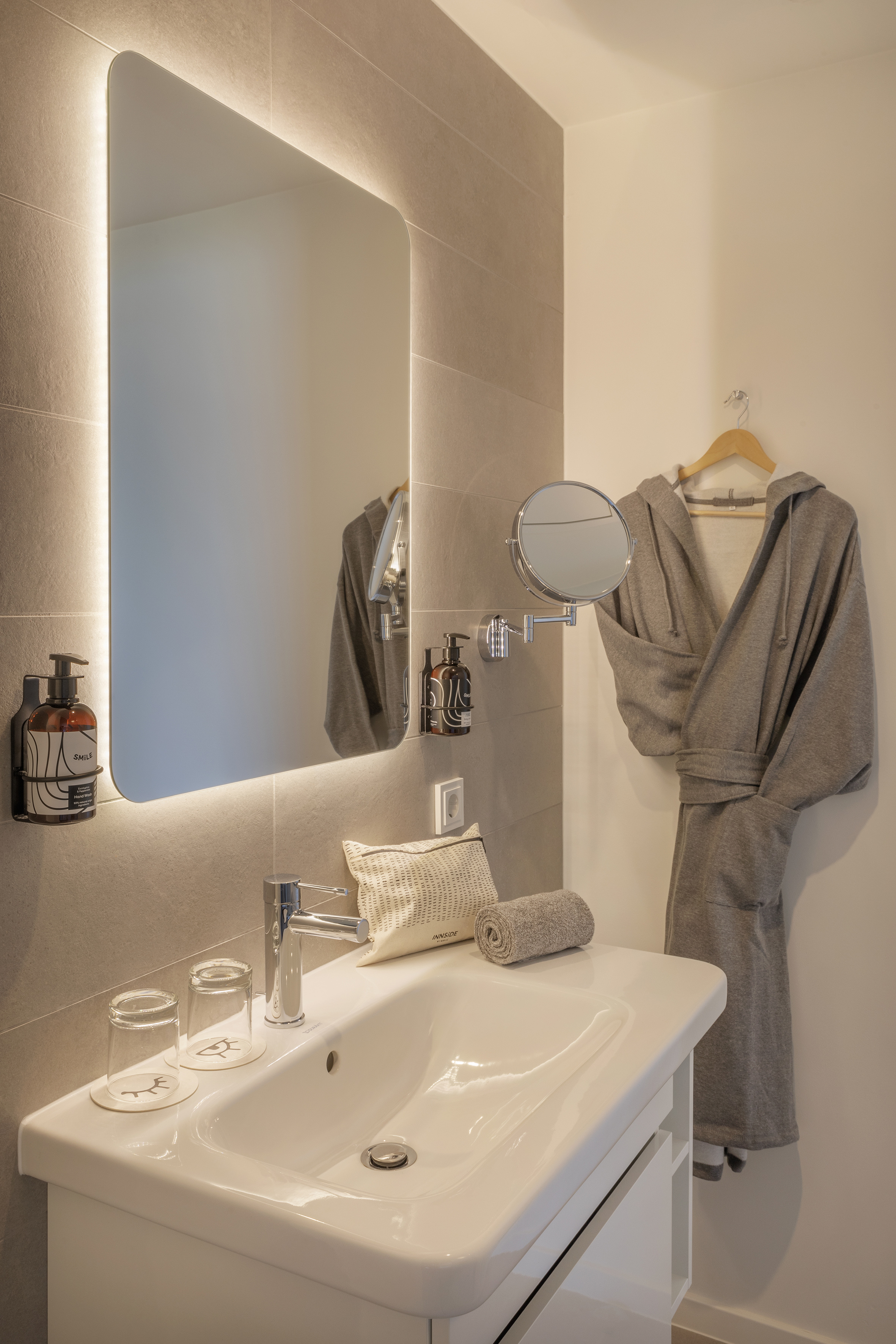 Modern hotel bathroom vanity with lighted mirror and grey bathrobe.
