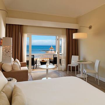 a room with a bed and a table and chairs and a beach view