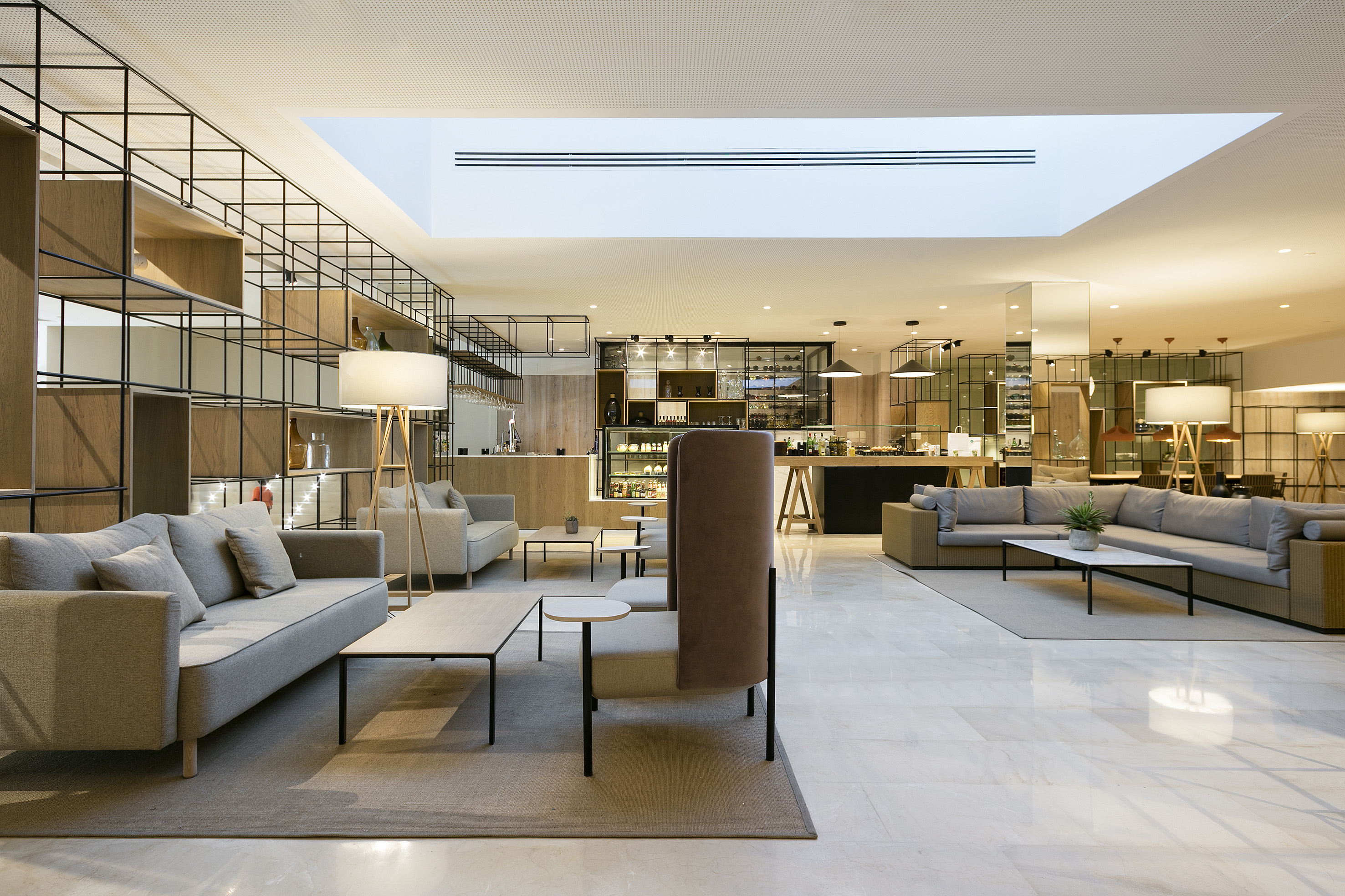 Modern hotel lobby lounge with grey sofas, sleek shelving, and bar area.