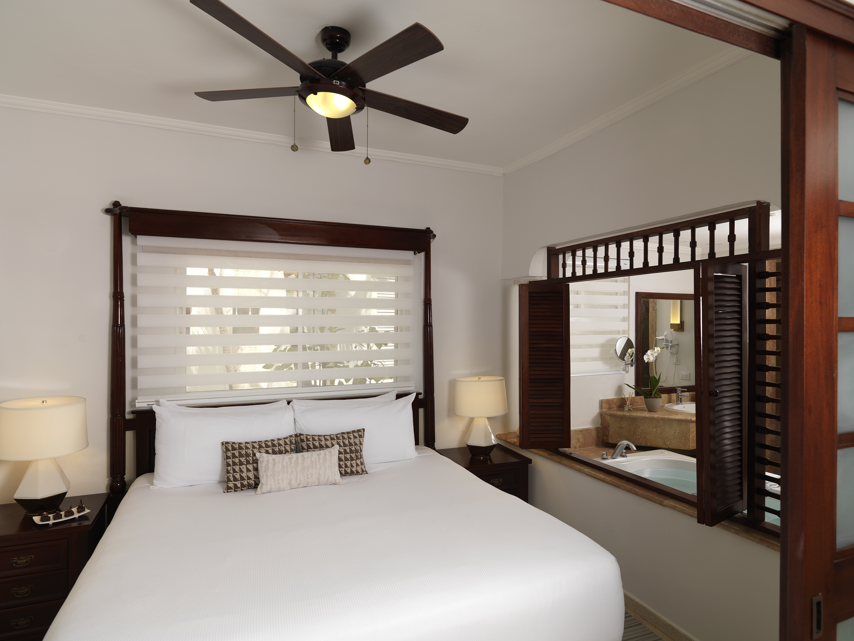 Bedroom with dark wood bed, ceiling fan, and open bathroom view with tub.
