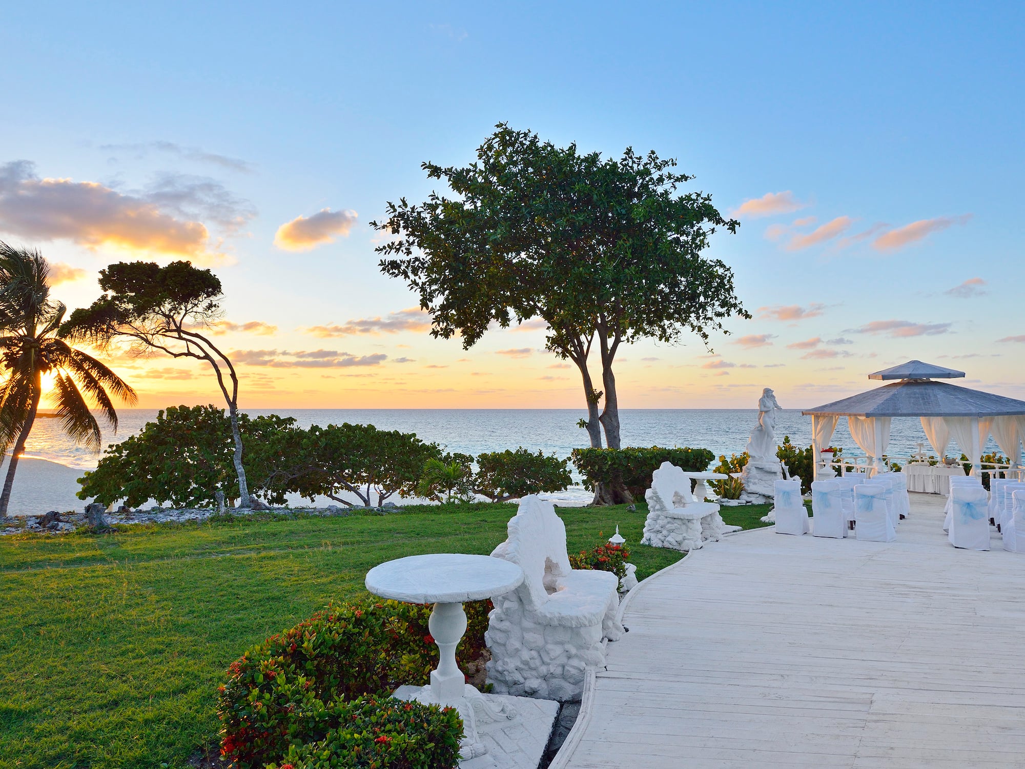 a white patio with a gazebo and trees and a sunset
