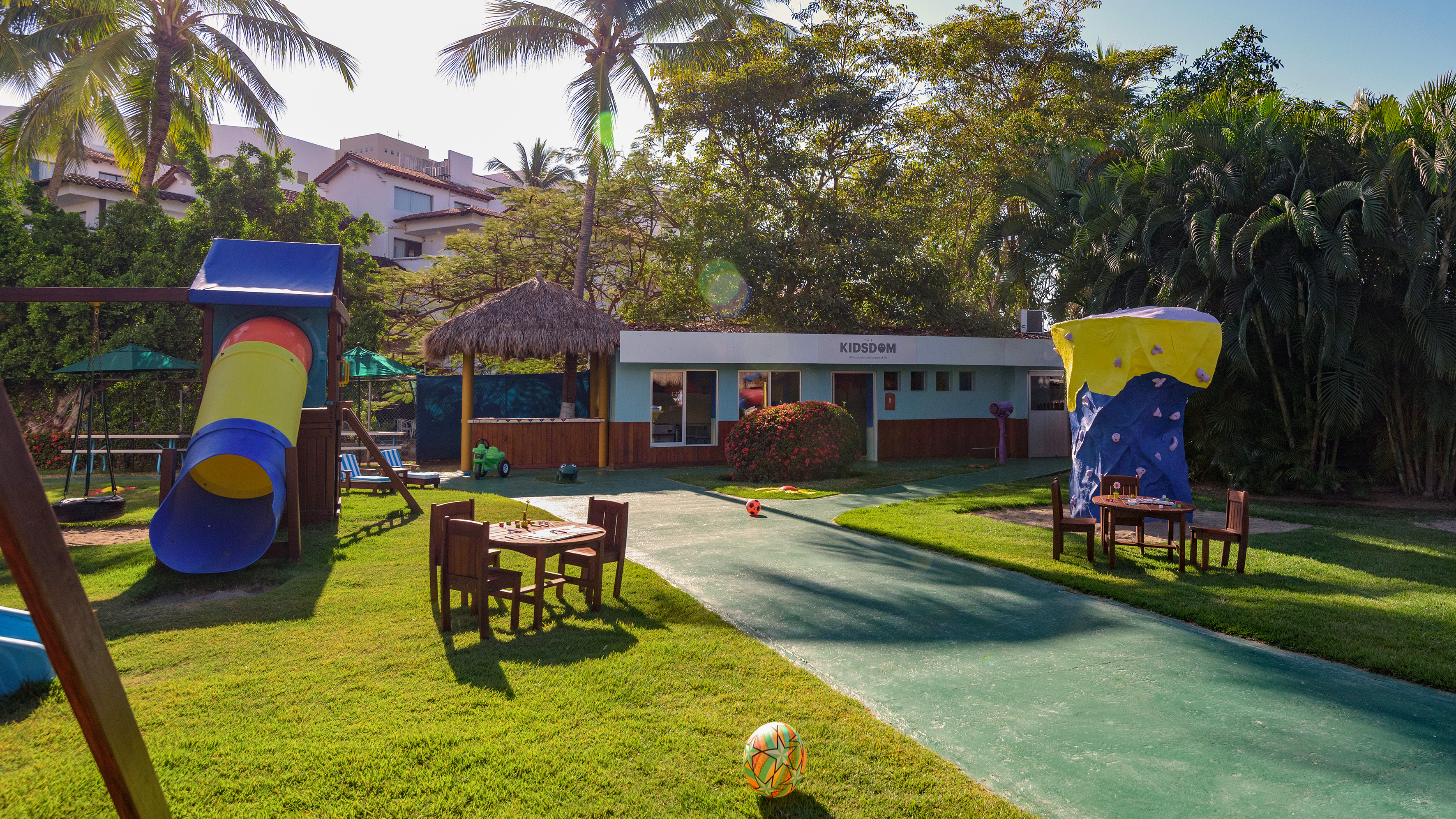 KIDSDOM kids club with slide, rock climbing wall, and tropical playground.