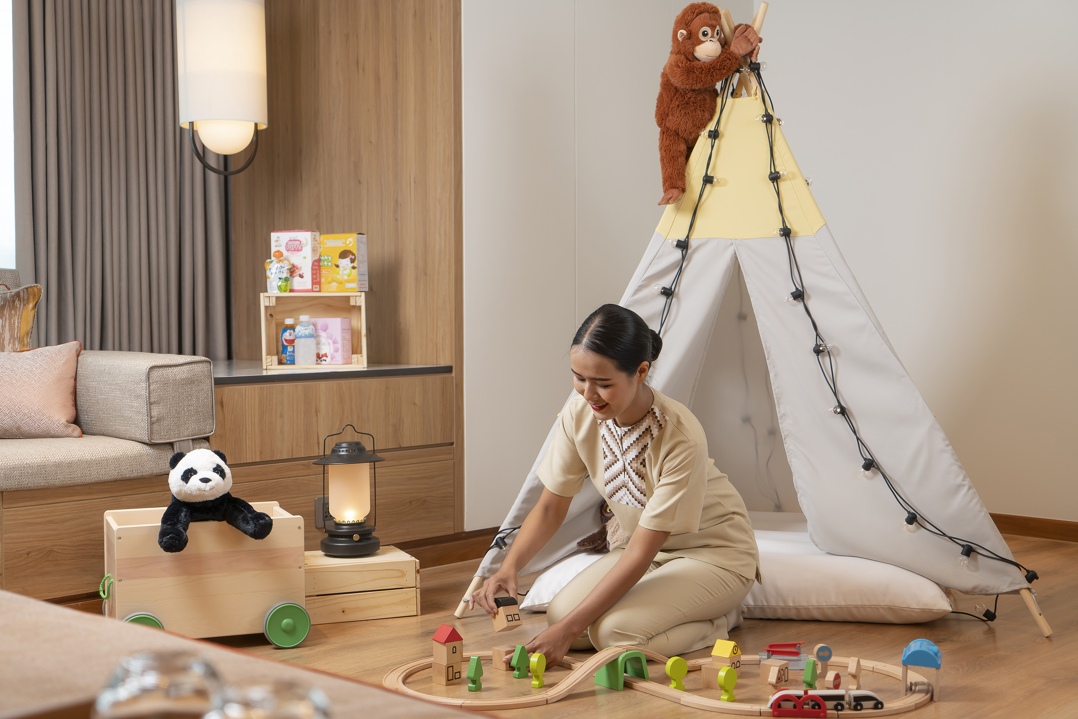 Hotel staff playing with wooden train set in family-friendly kids' room.