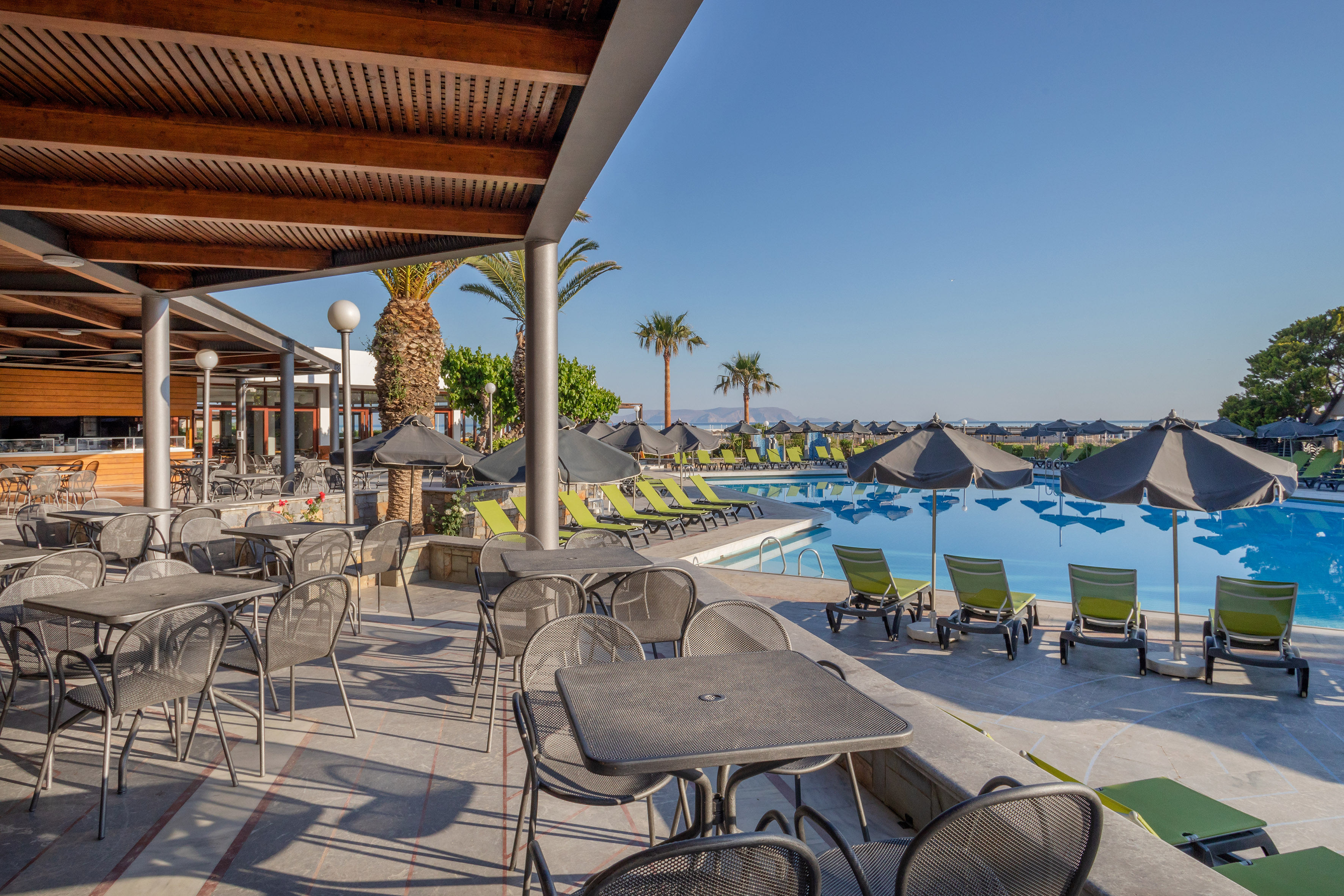 Outdoor restaurant patio and resort pool area with lounge chairs, palm trees.