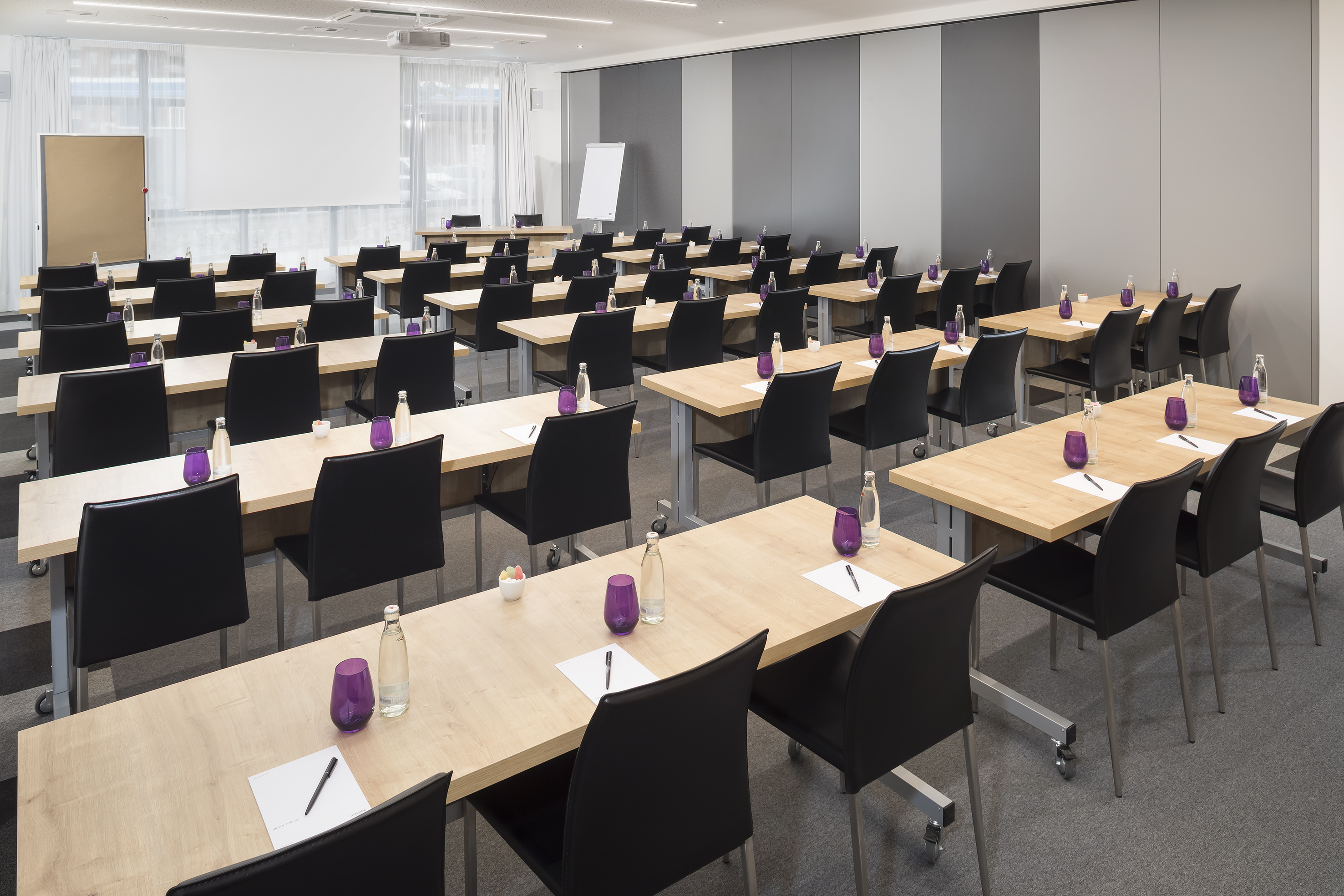 Modern training room with tables, black chairs, water, and notepads.