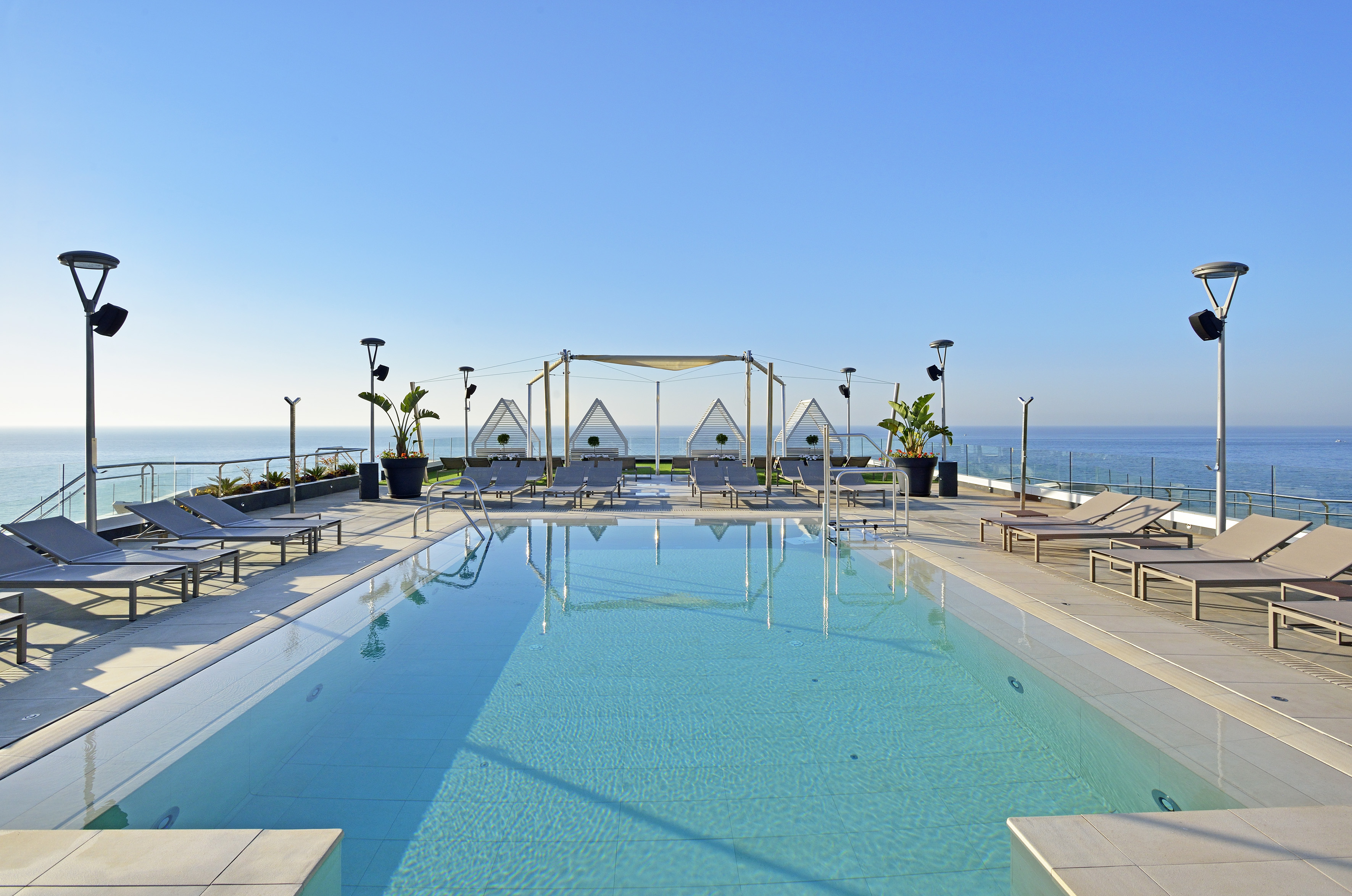 Rooftop swimming pool with ocean view, sunbeds, and modern sun shades.