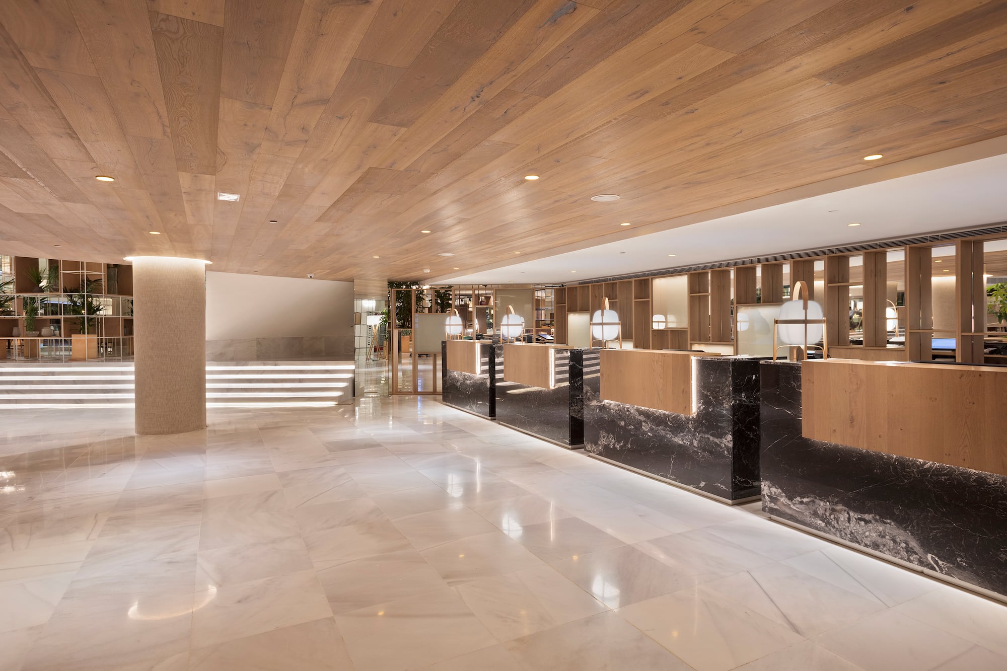 Modern hotel lobby with wooden ceiling, white marble floor, and reception desks.