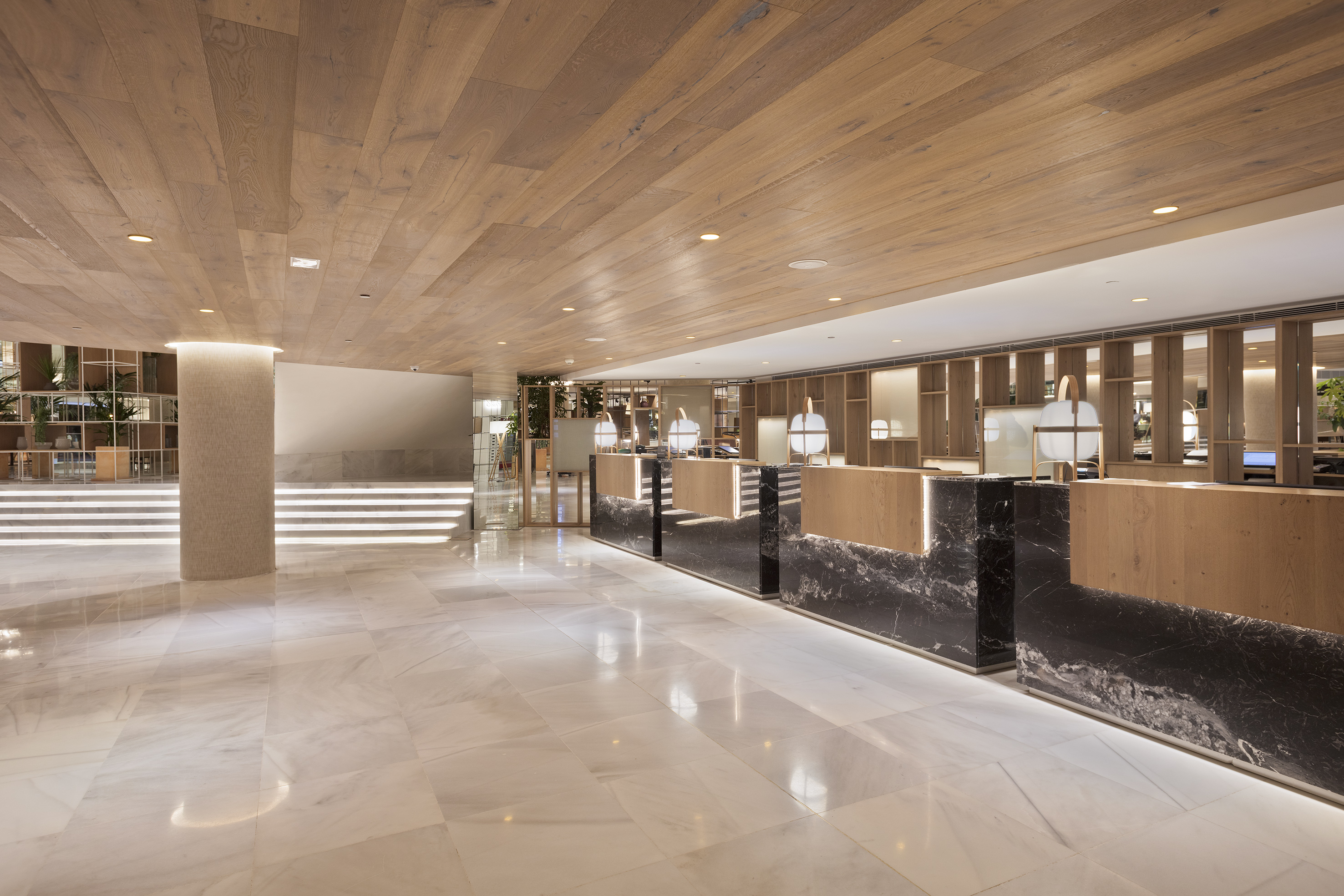 Modern hotel lobby with wooden ceiling, white marble floor, and reception desks.