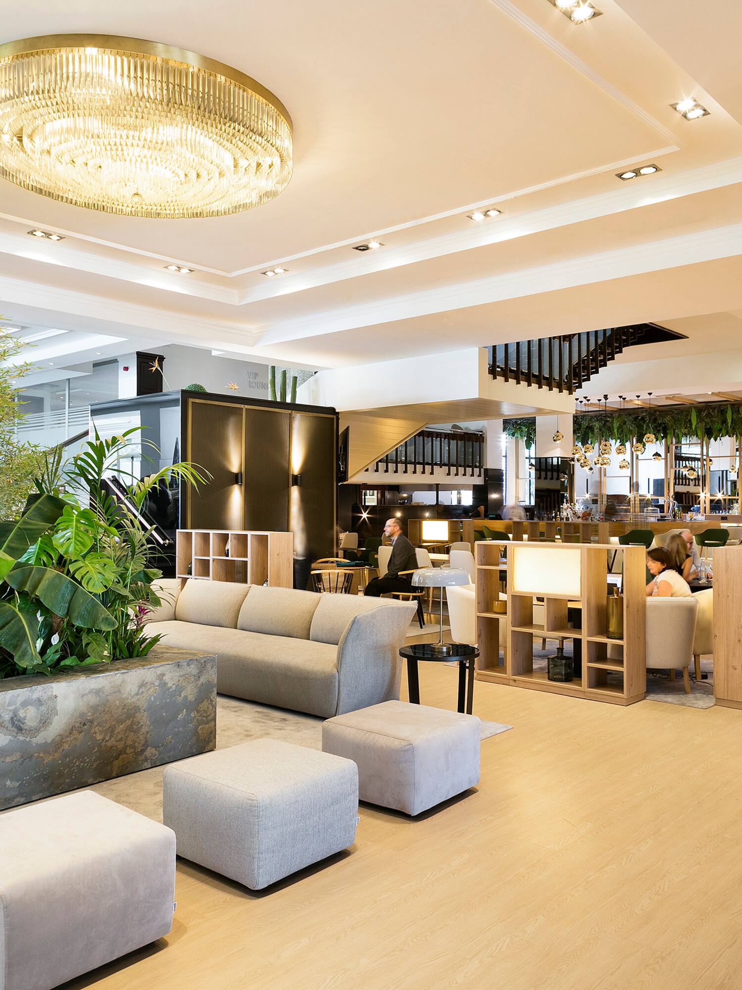 Luxurious hotel lounge with lush plants, modern sofas, and gold chandelier.
