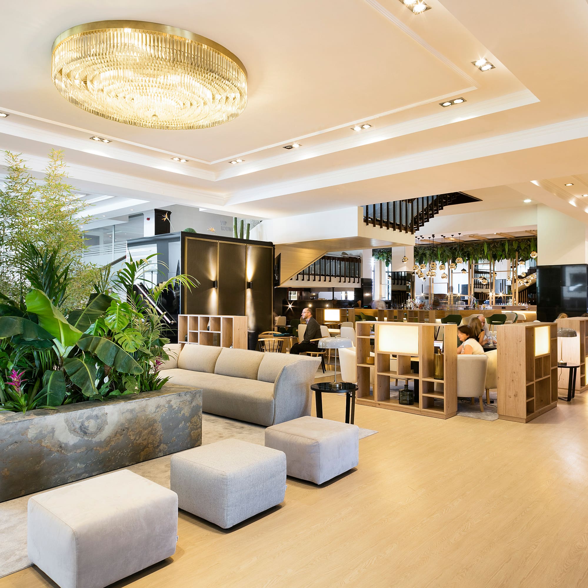 Luxury hotel lobby with modern seating, lush plants, and a grand chandelier.