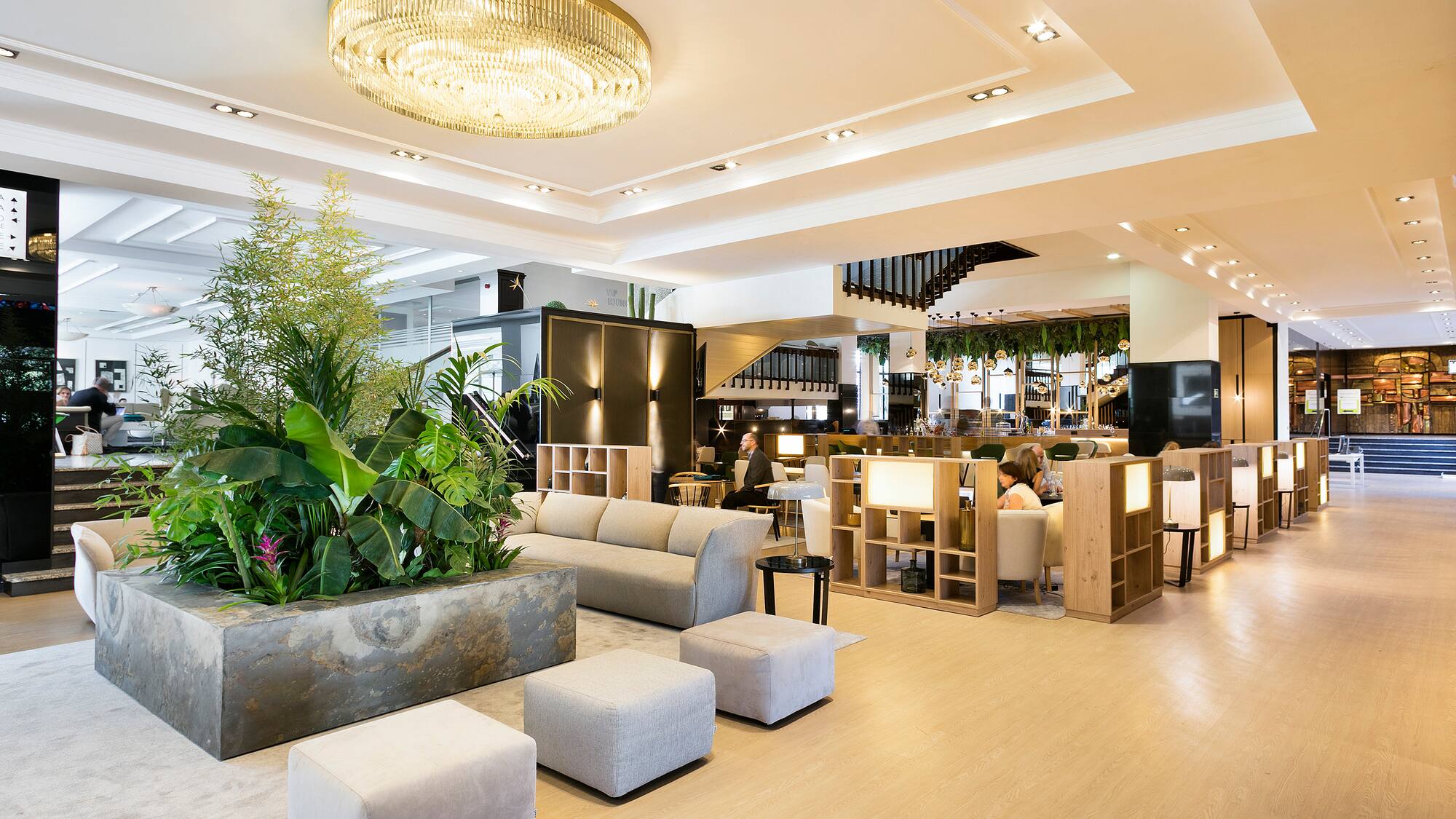 Luxury hotel lobby with modern seating, lush plants, and a grand chandelier.