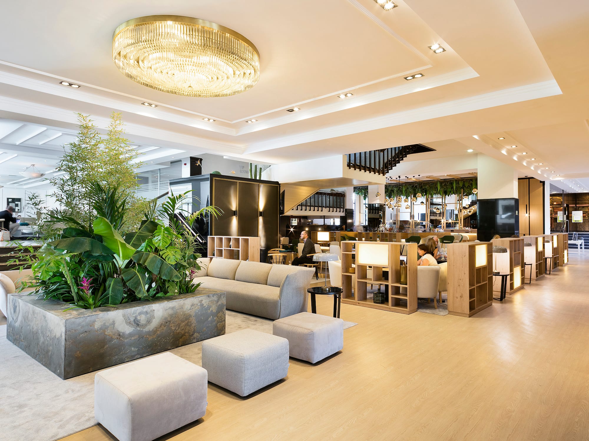 Contemporary hotel lobby with large chandelier, plants, and lounge seating.