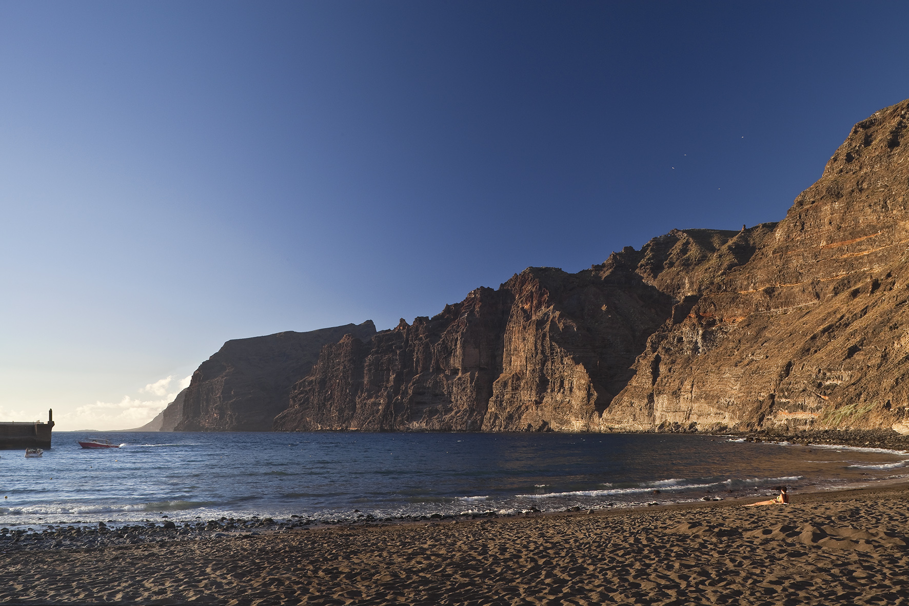 Los Gigantes cliffs, dark sand beach, and blue ocean under golden hour sun.