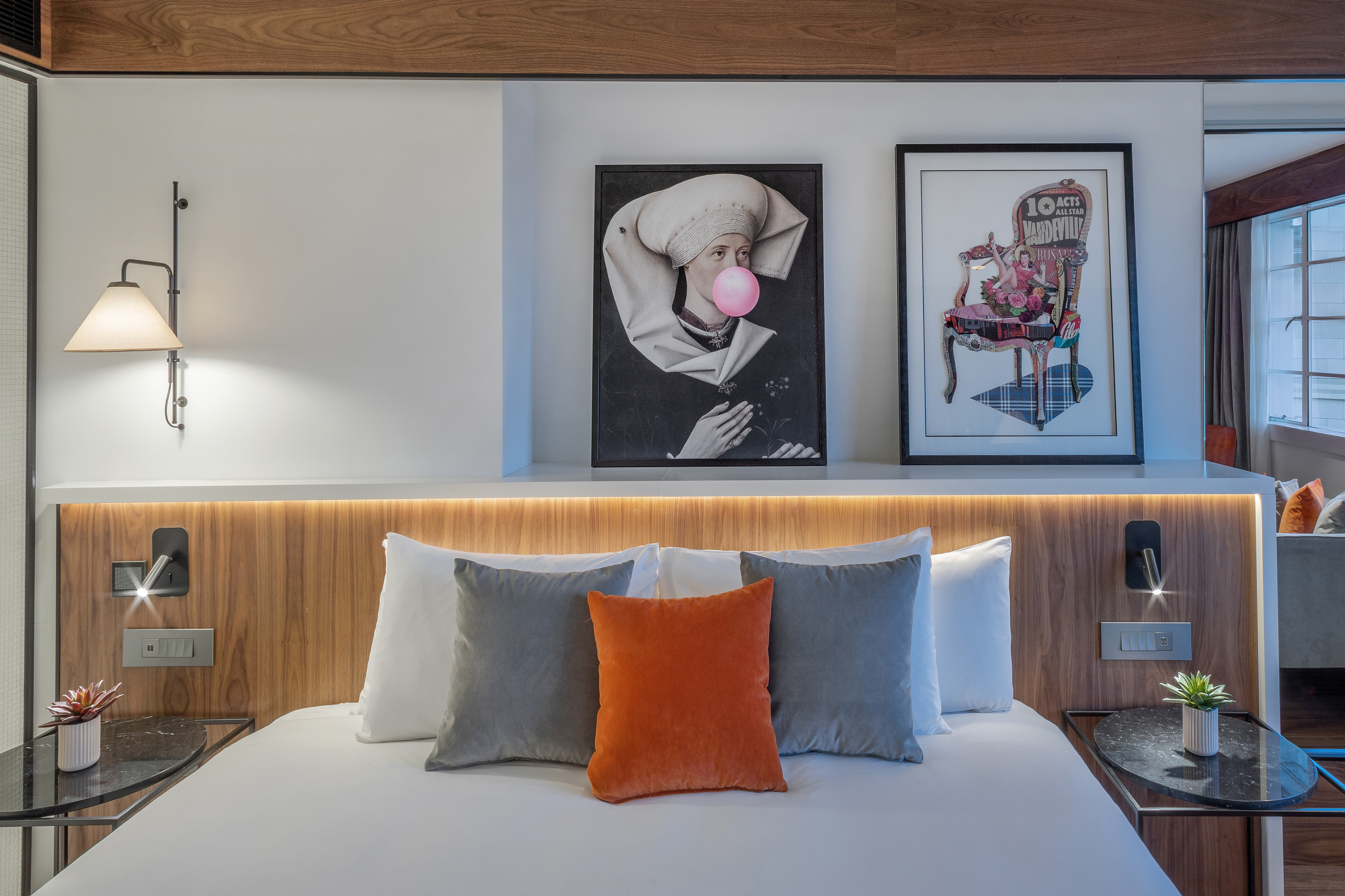 Modern hotel bedroom with wooden headboard, eclectic wall art, and cozy lighting.
