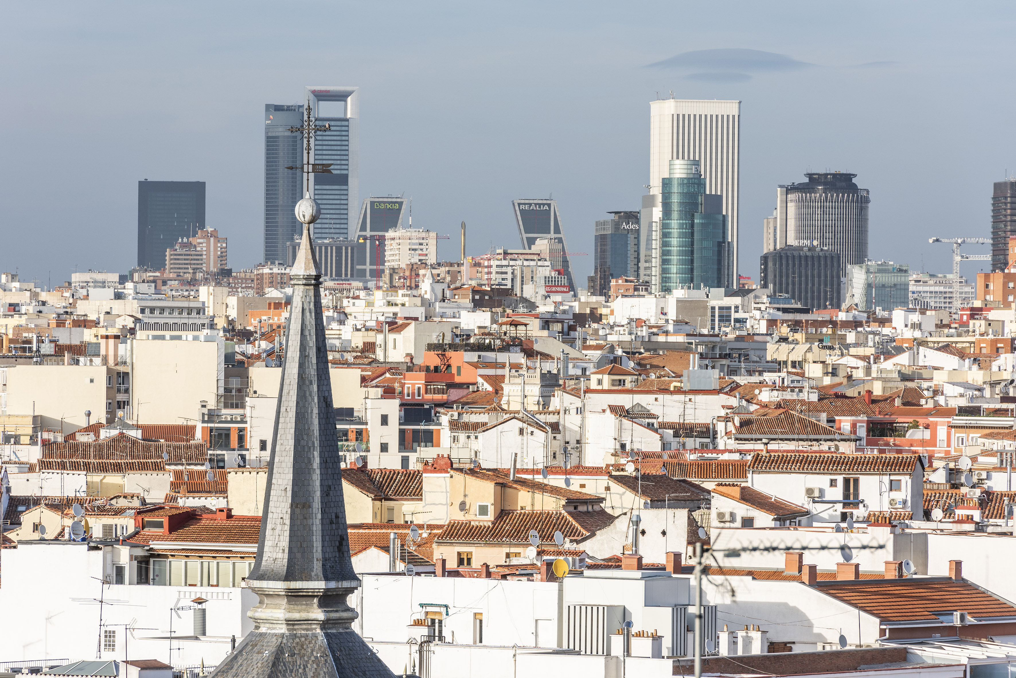 Madrid cityscape: Old church spire and tiled roofs before modern skyscrapers.