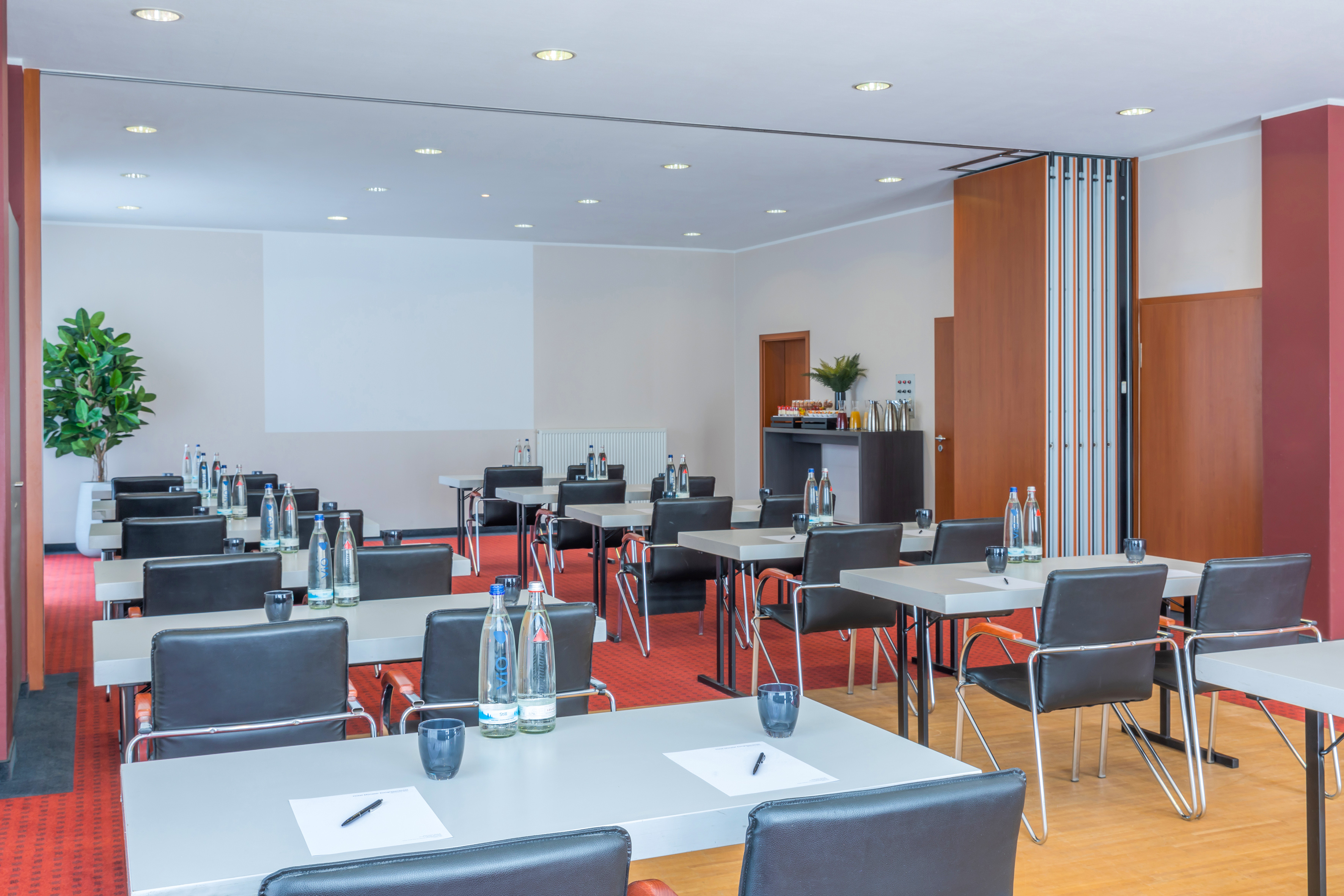 Conference room set with tables, chairs, water bottles, and a screen.