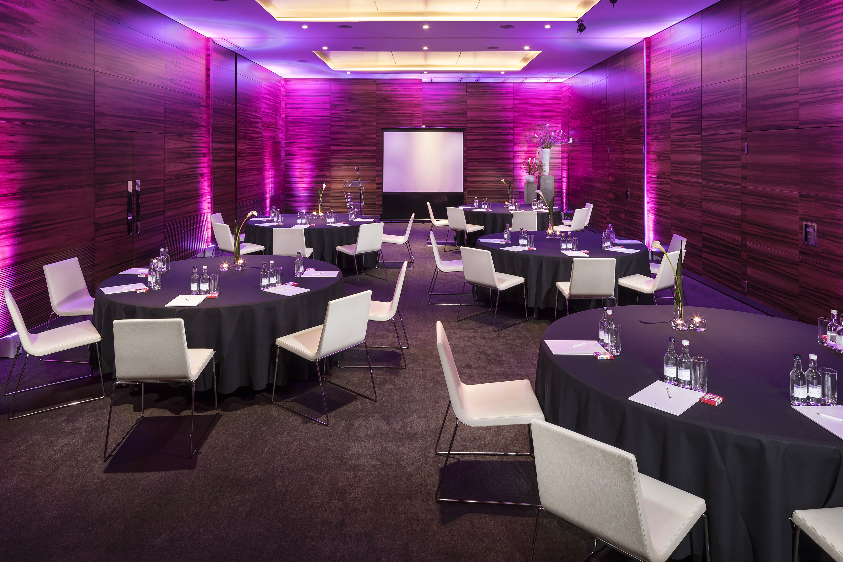 Elegant event space with black tables, white chairs, and purple wall lighting.