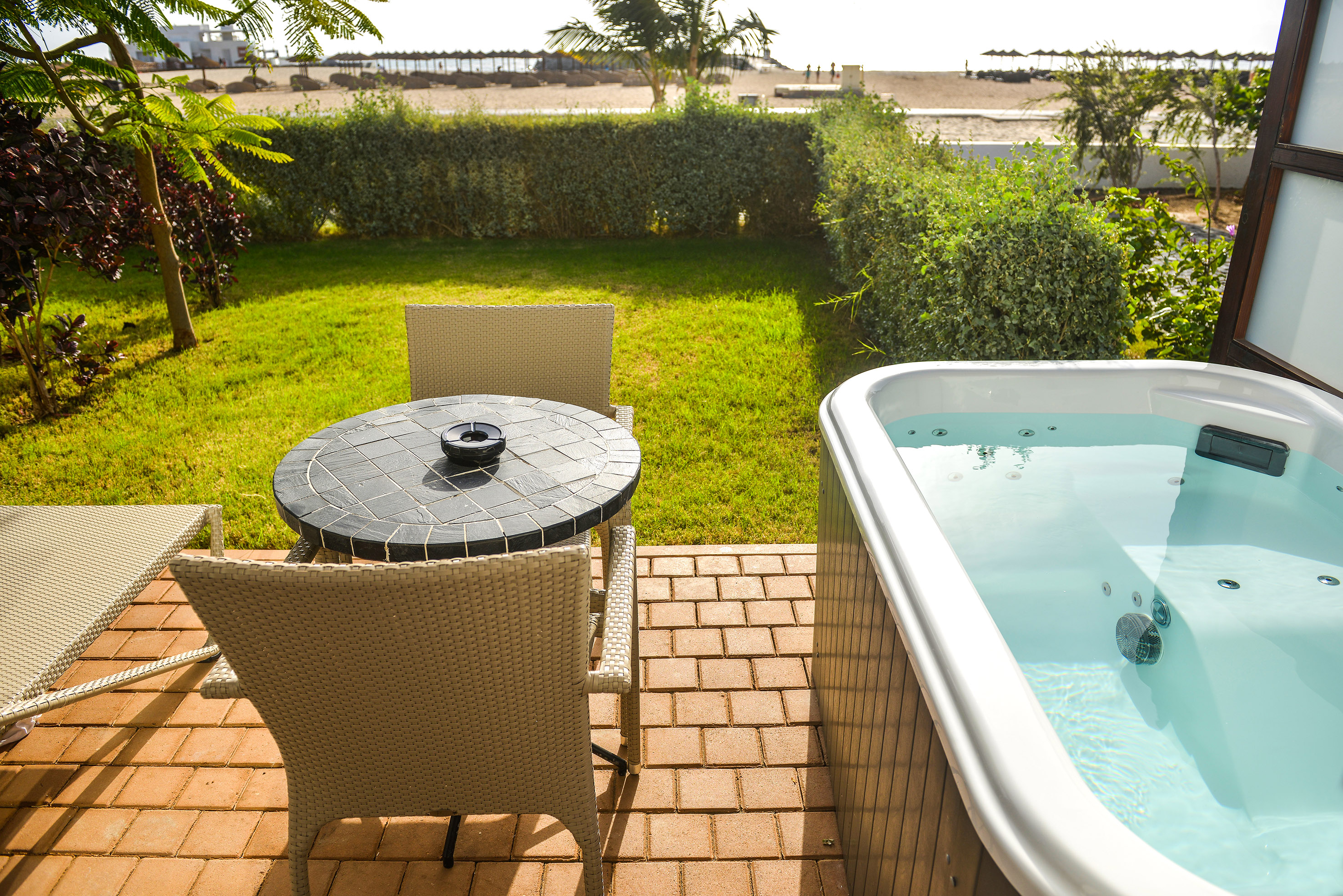 a table and chair on a patio with a hot tub and a beach in the background