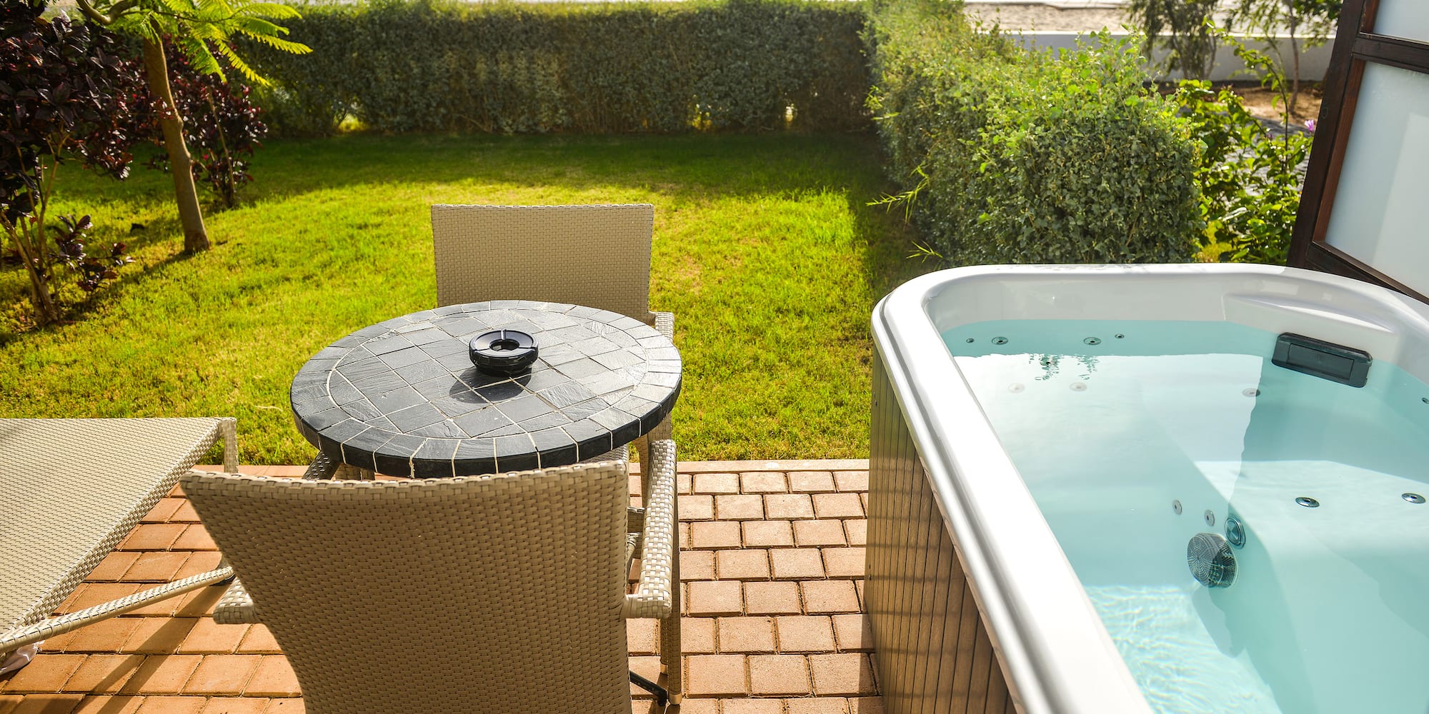 a table and chair on a patio with a hot tub and a beach in the background