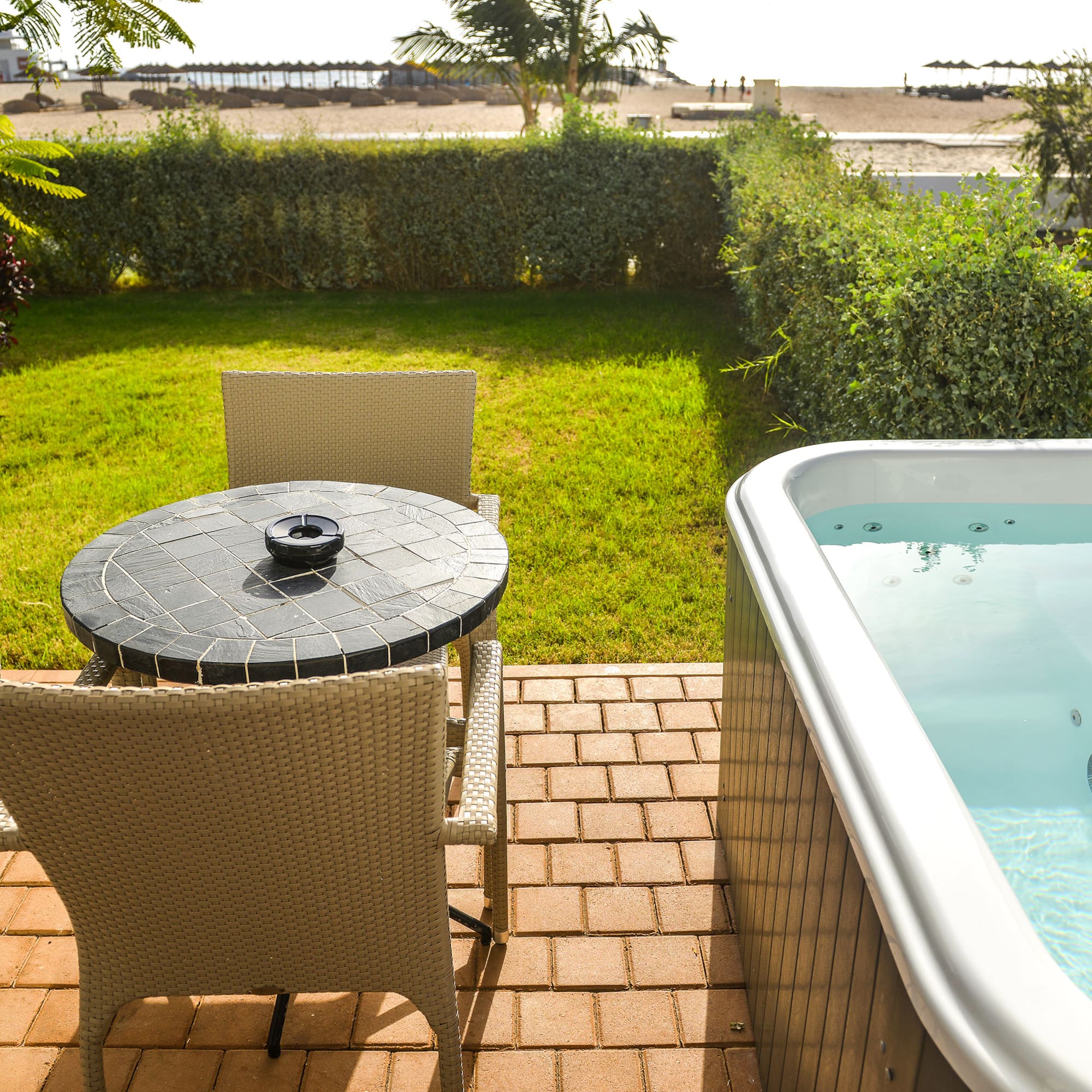 a table and chair on a patio with a hot tub and a beach in the background