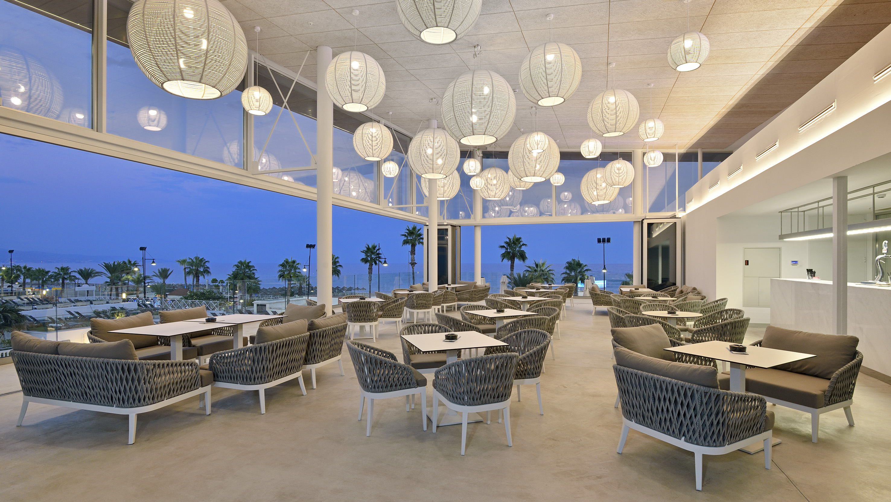 Modern restaurant lounge with sea view and woven pendant lights.