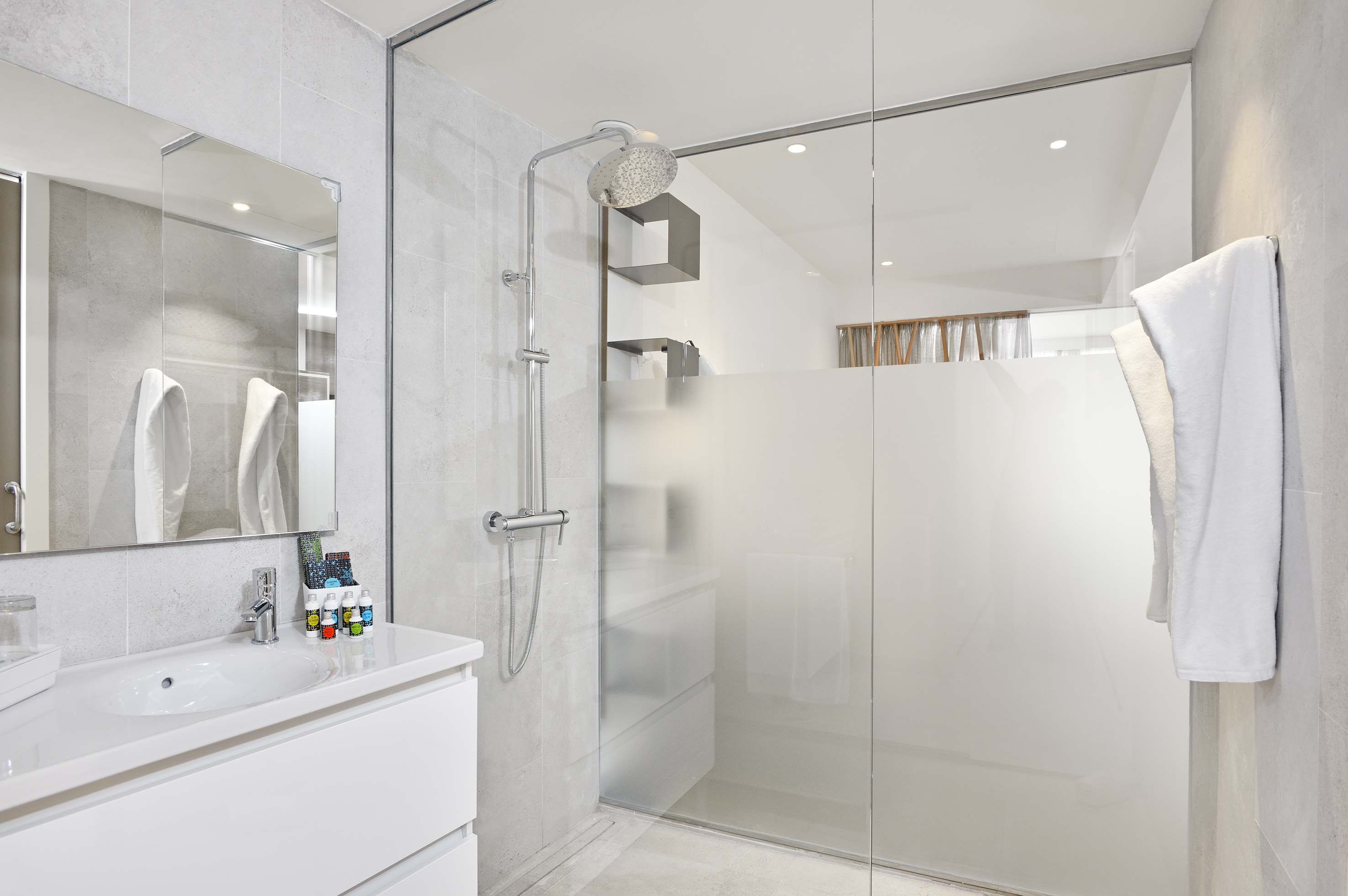 Modern white bathroom with walk-in shower, sleek vanity, and grey tiles.