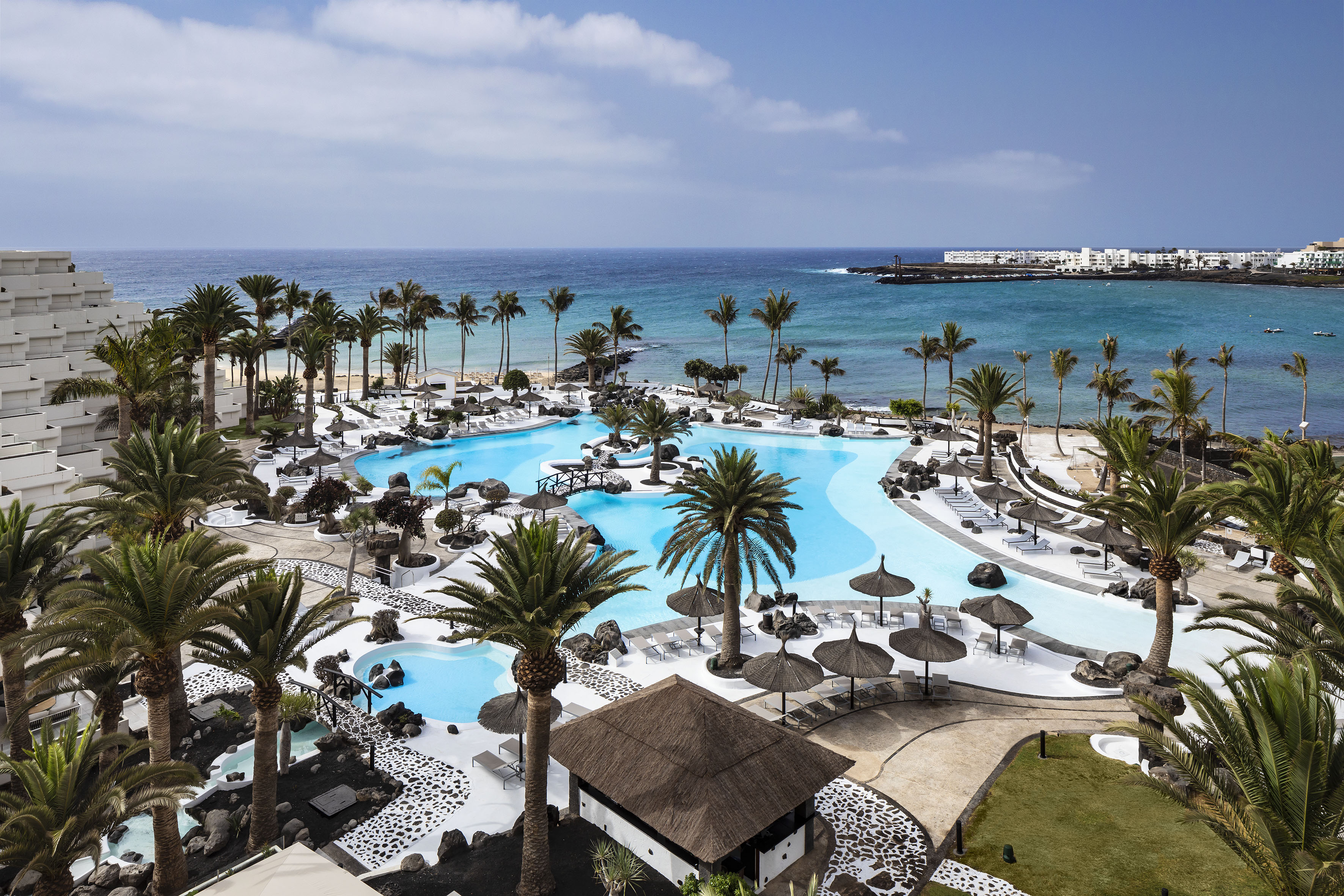 Aerial view of a tropical resort with lagoon pools, palm trees, and ocean.