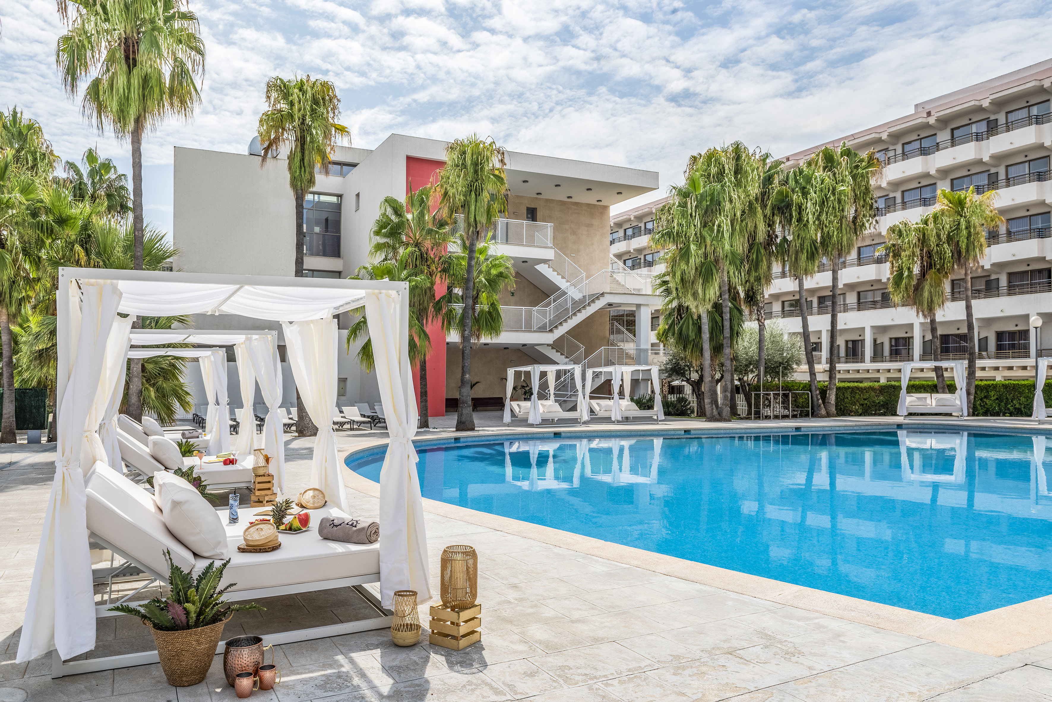 Luxury hotel pool with white cabanas, palm trees, and modern buildings.
