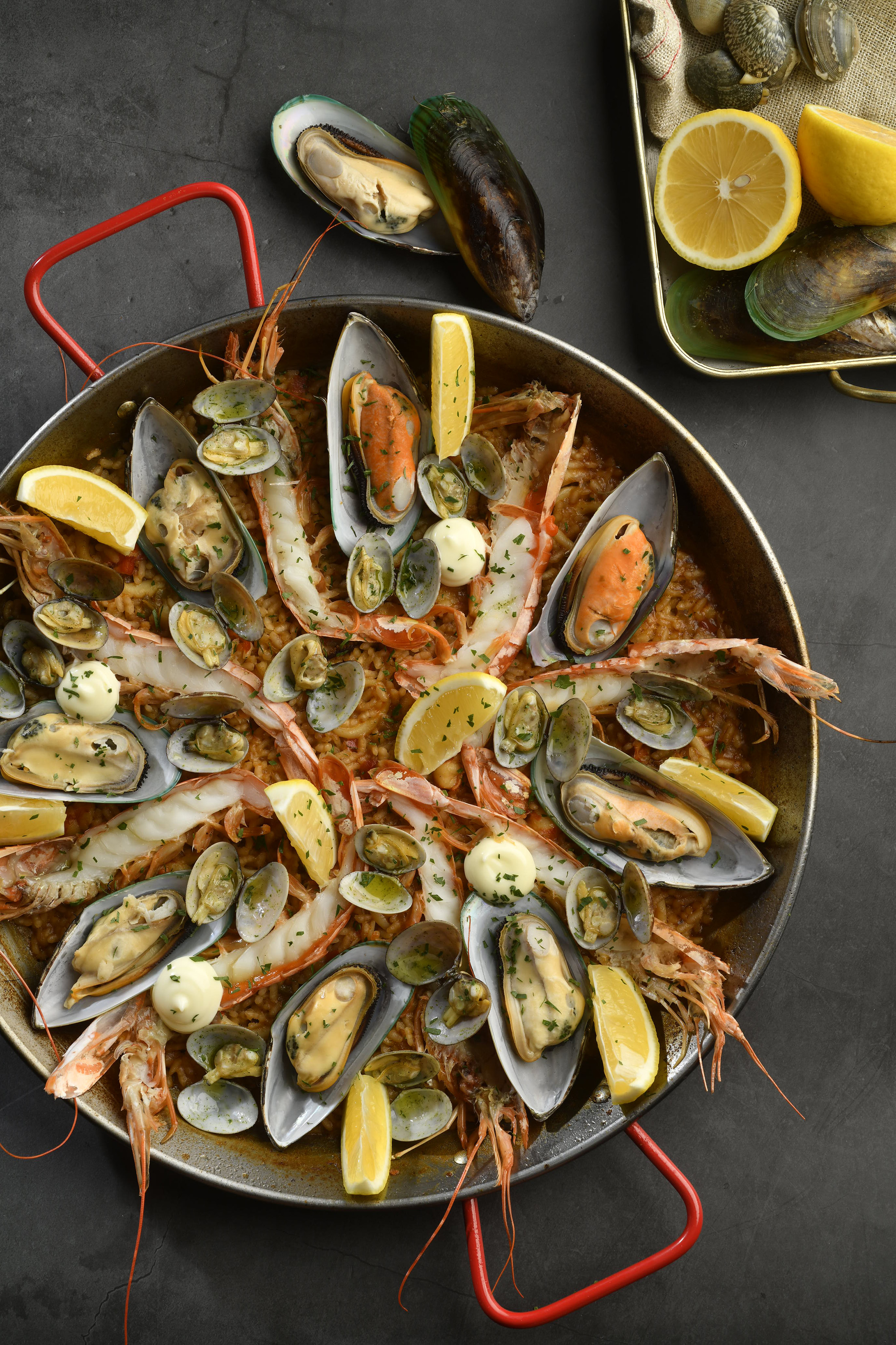 Paella pan with shrimp, mussels, clams, rice, lemon, and aioli.