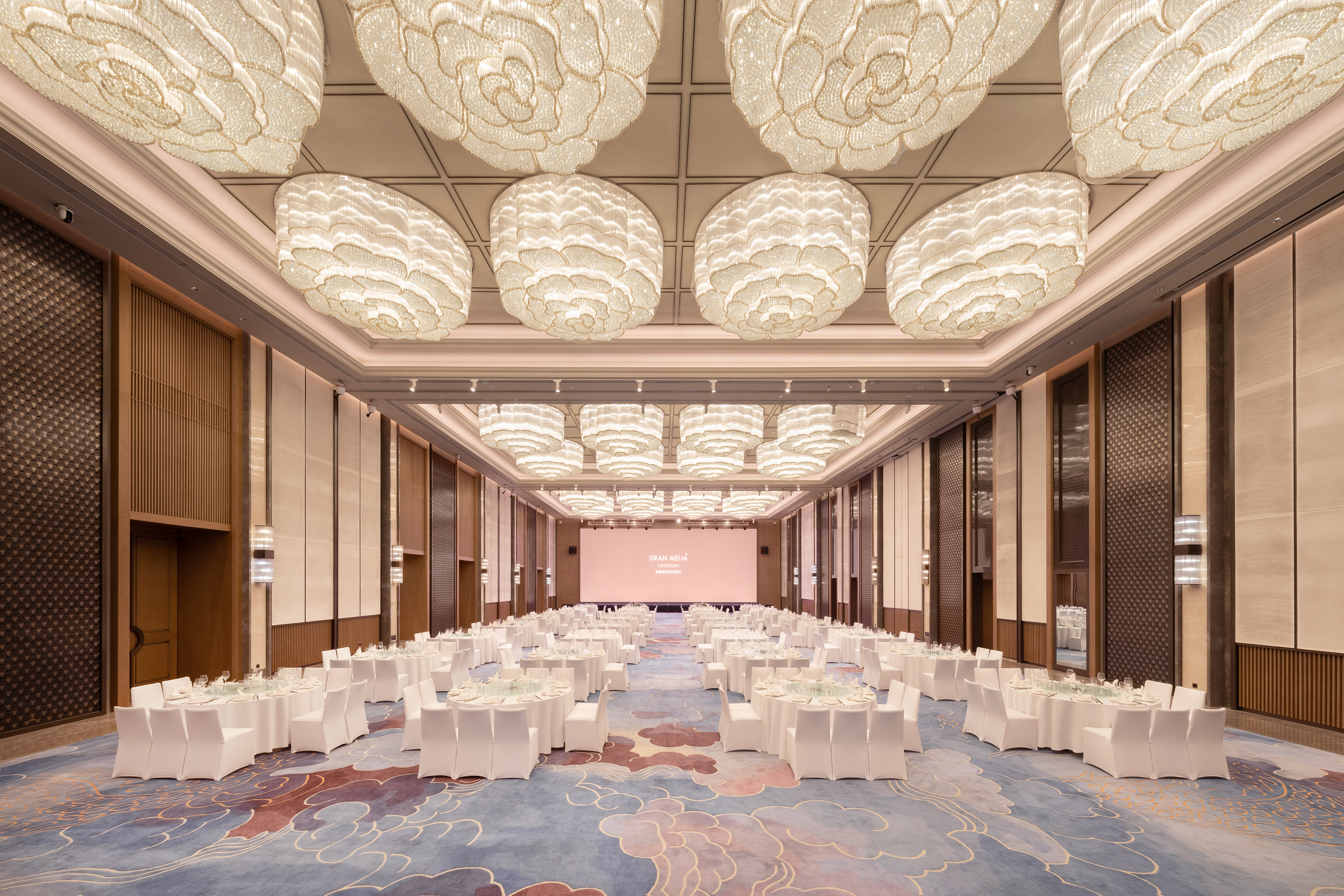 Grand hotel ballroom with banquet setup, white tables, and elegant chandeliers.