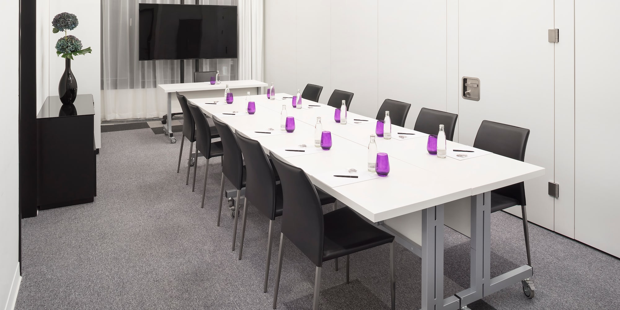 a long conference room with white tables and purple glasses