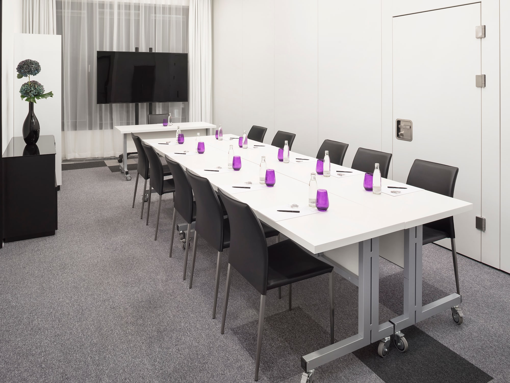 a long conference room with white tables and purple glasses