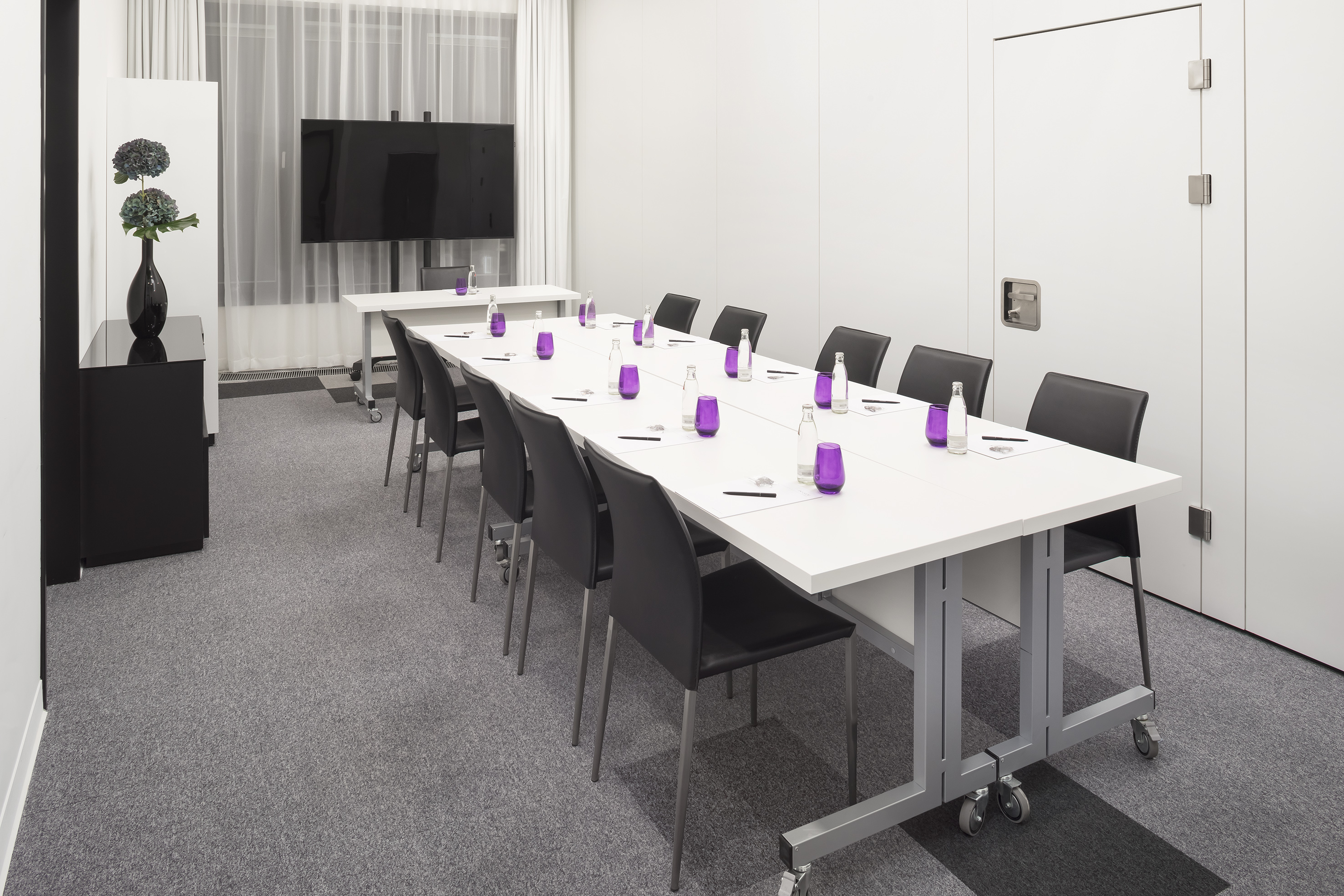 Modern conference room with white table, black chairs, and large display screen.