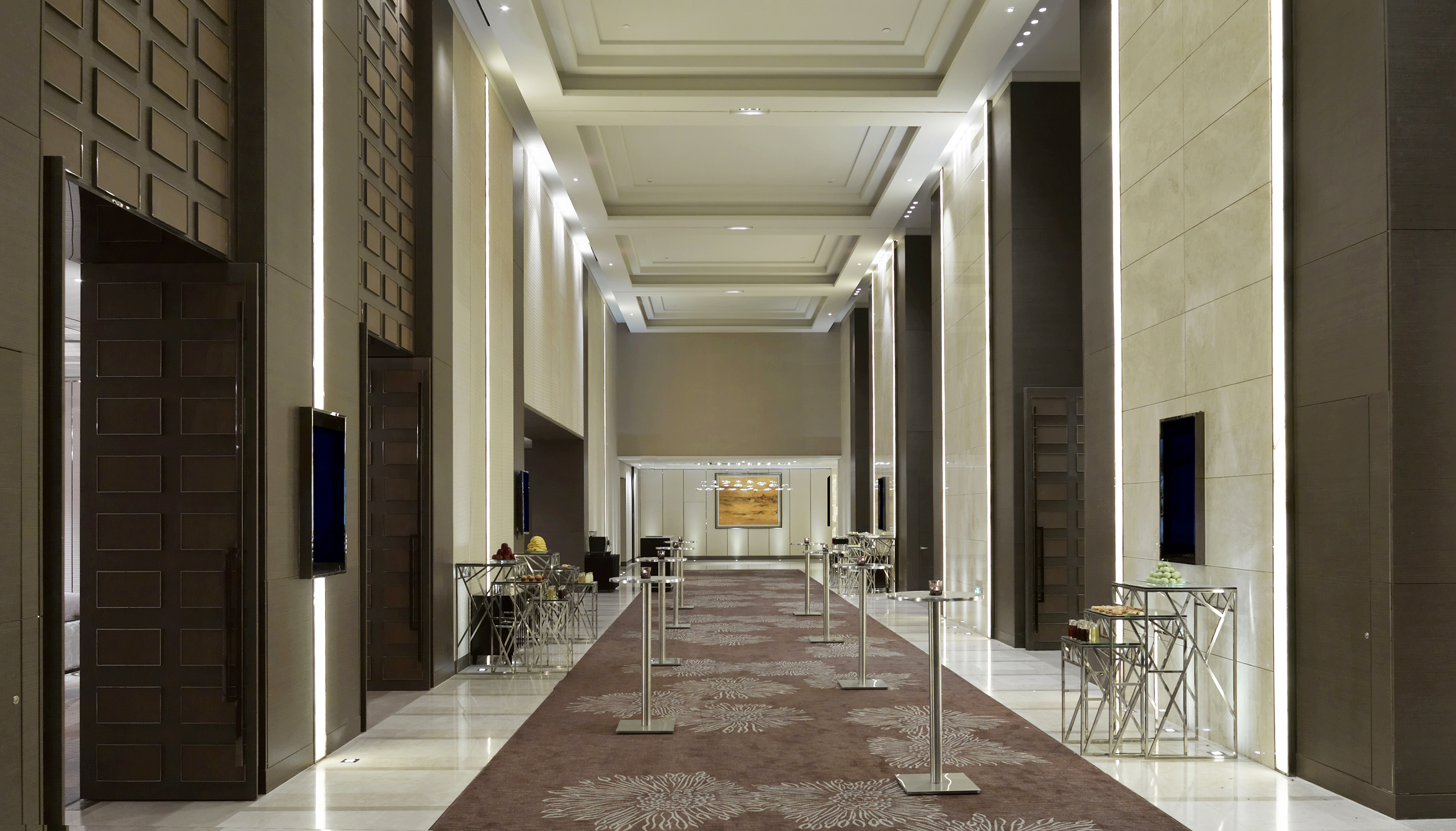 Modern luxury event corridor with vertical lighting and reception tables.