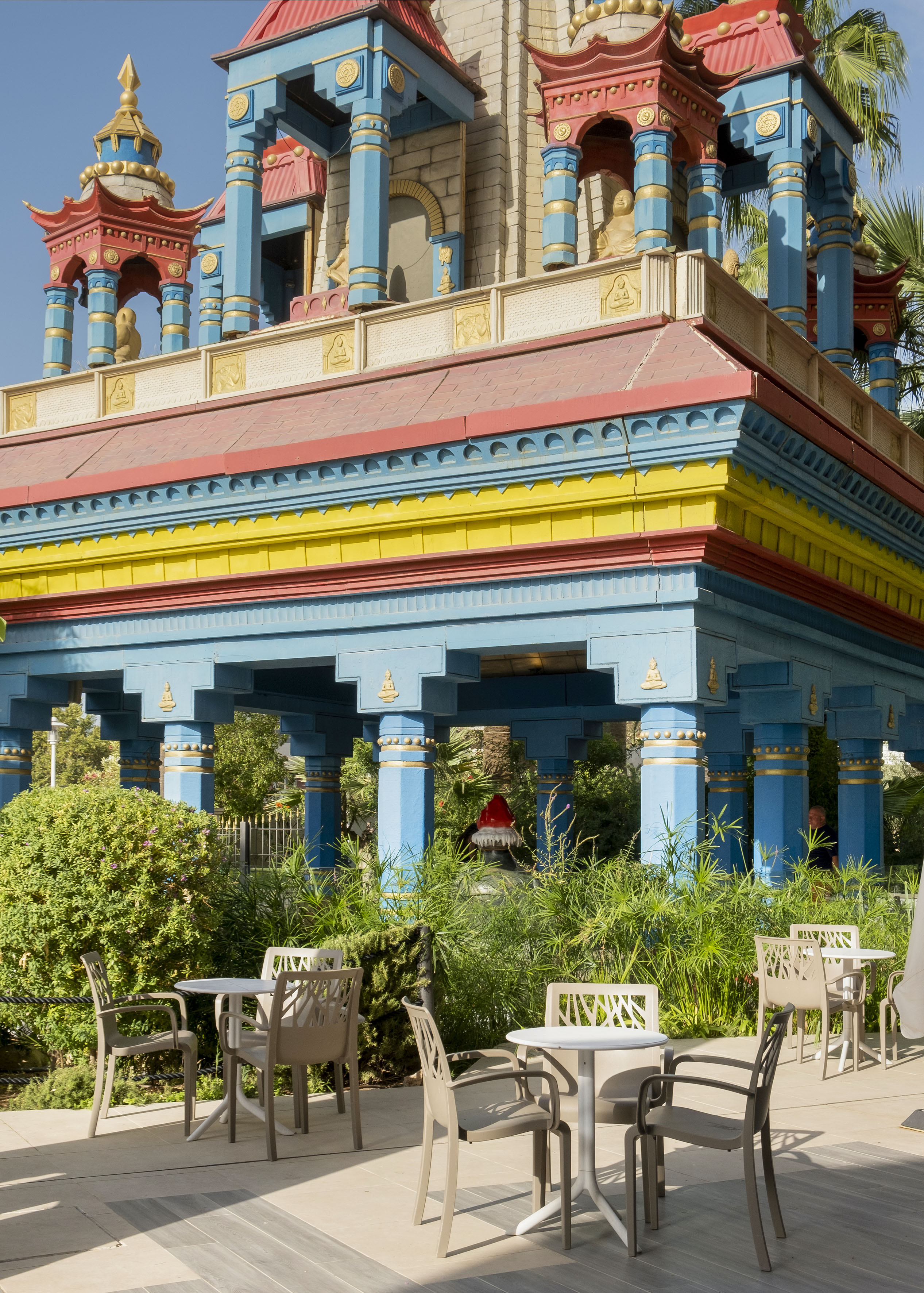 Colorful temple architecture with Buddha statues and outdoor garden cafe seating.