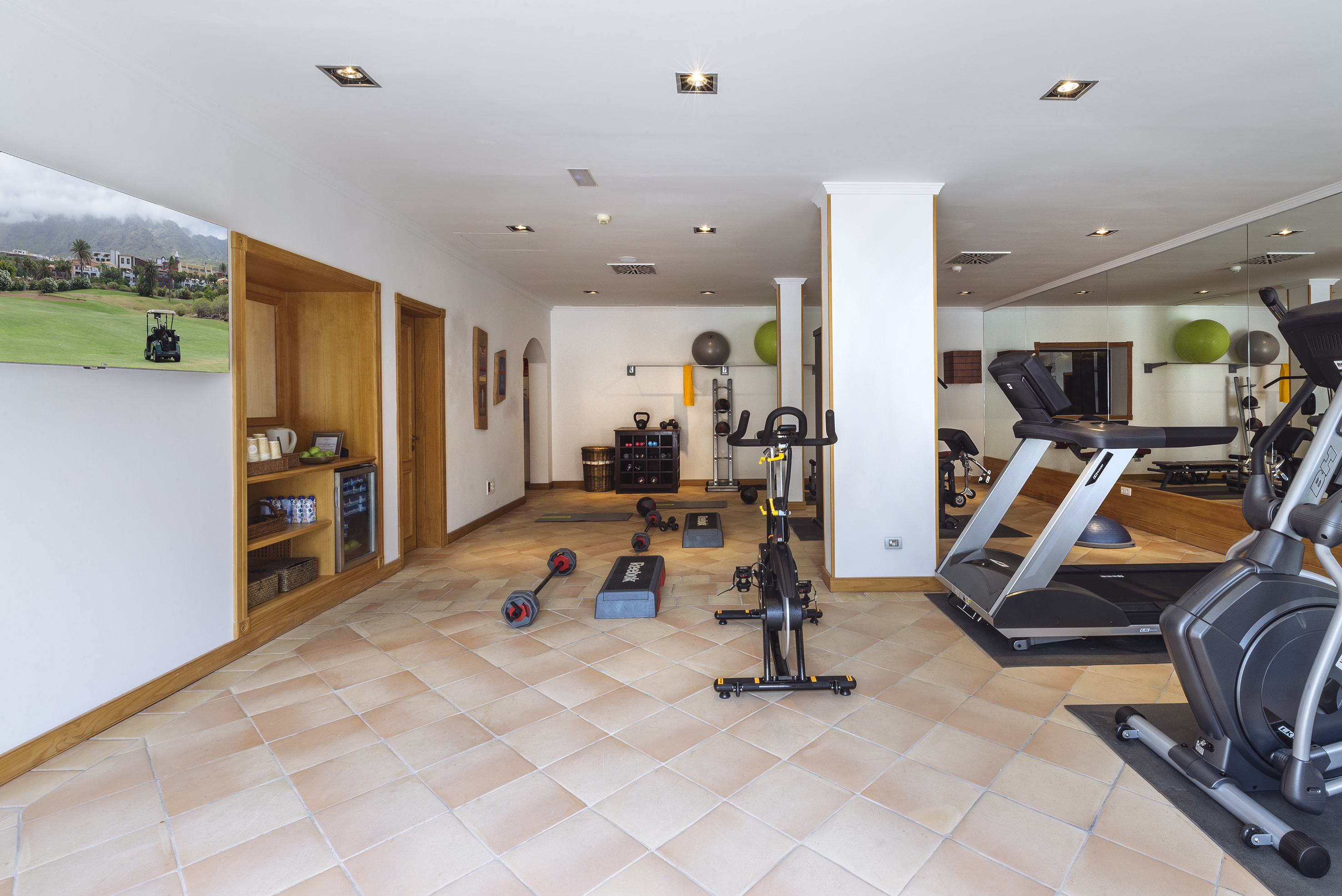 Indoor gym with treadmill, elliptical, spin bike, dumbbells, and fitness equipment.