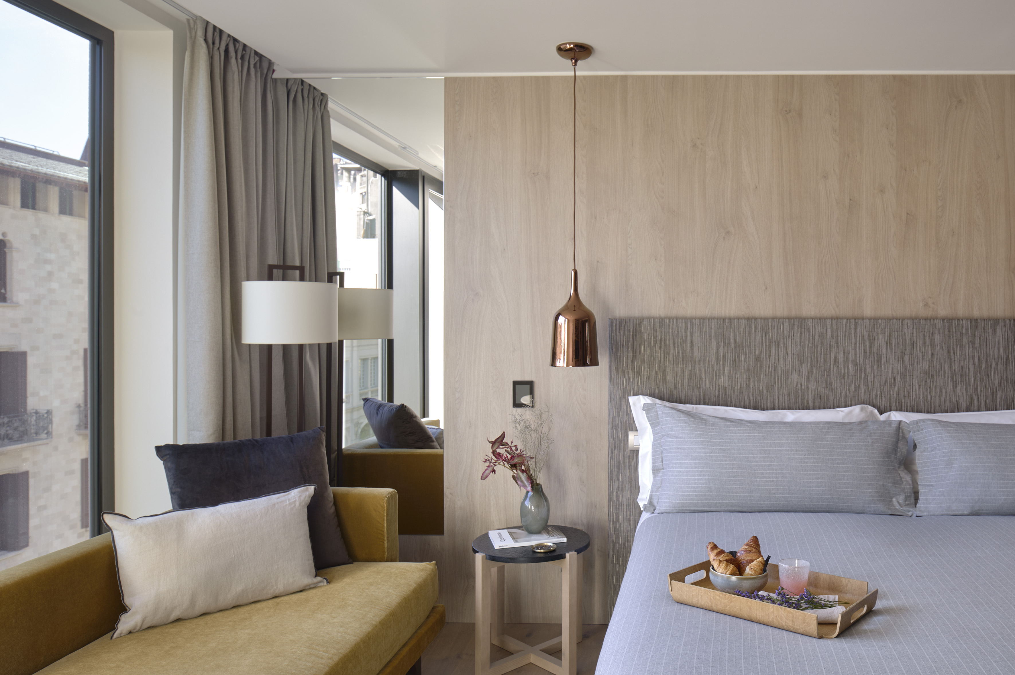 Stylish modern hotel bedroom with gray bed, breakfast tray, wood wall, city view.
