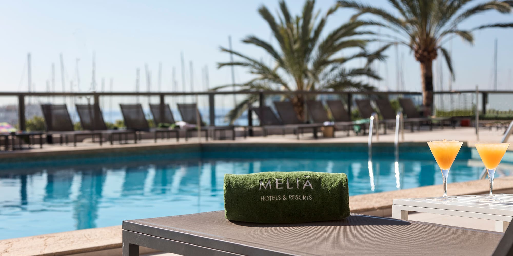 Meliá Hotels & Resorts pool with branded towel, cocktails, lounge chairs, and palm trees.