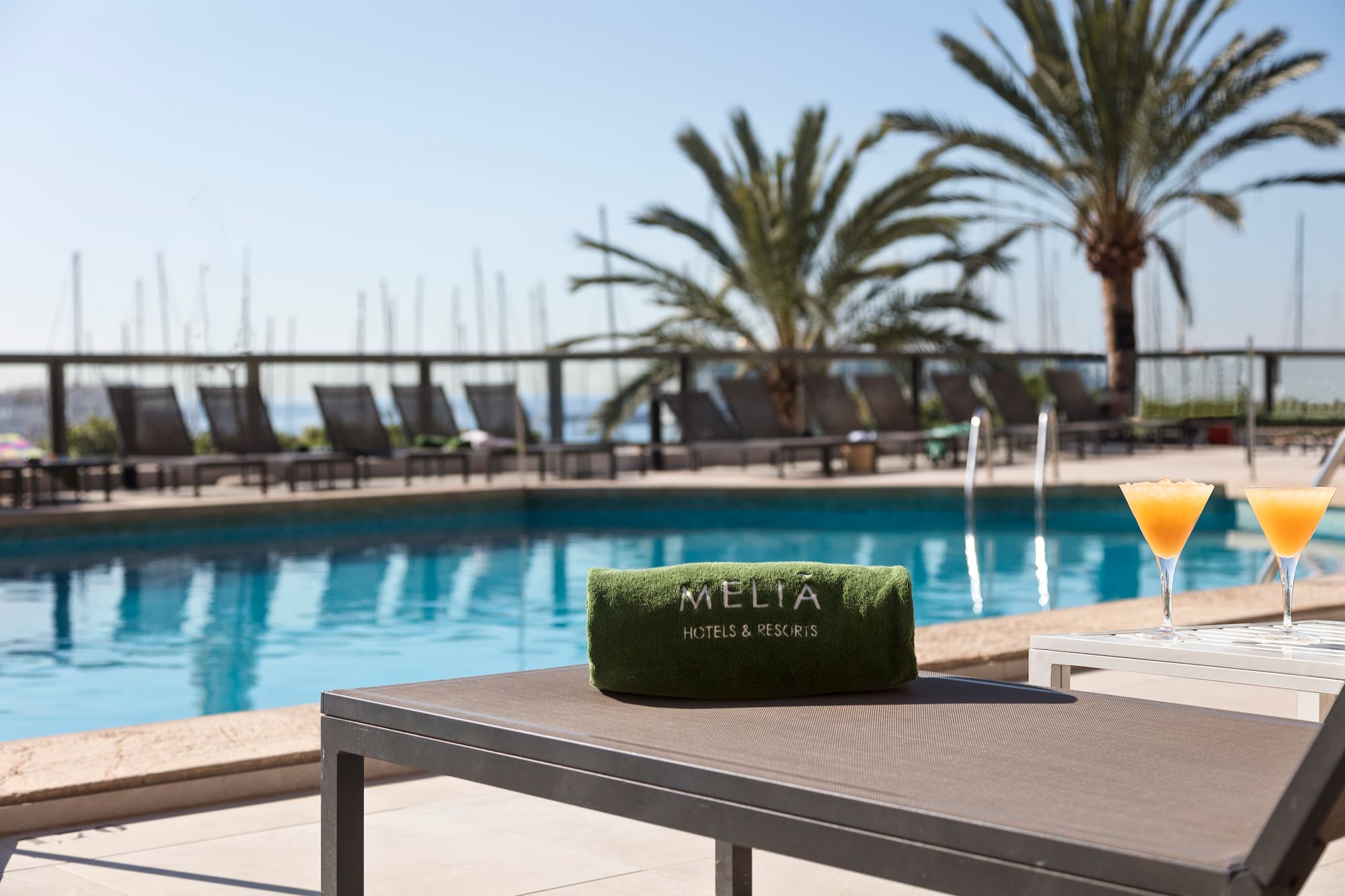 Meliá Hotels & Resorts pool with branded towel, cocktails, lounge chairs, and palm trees.