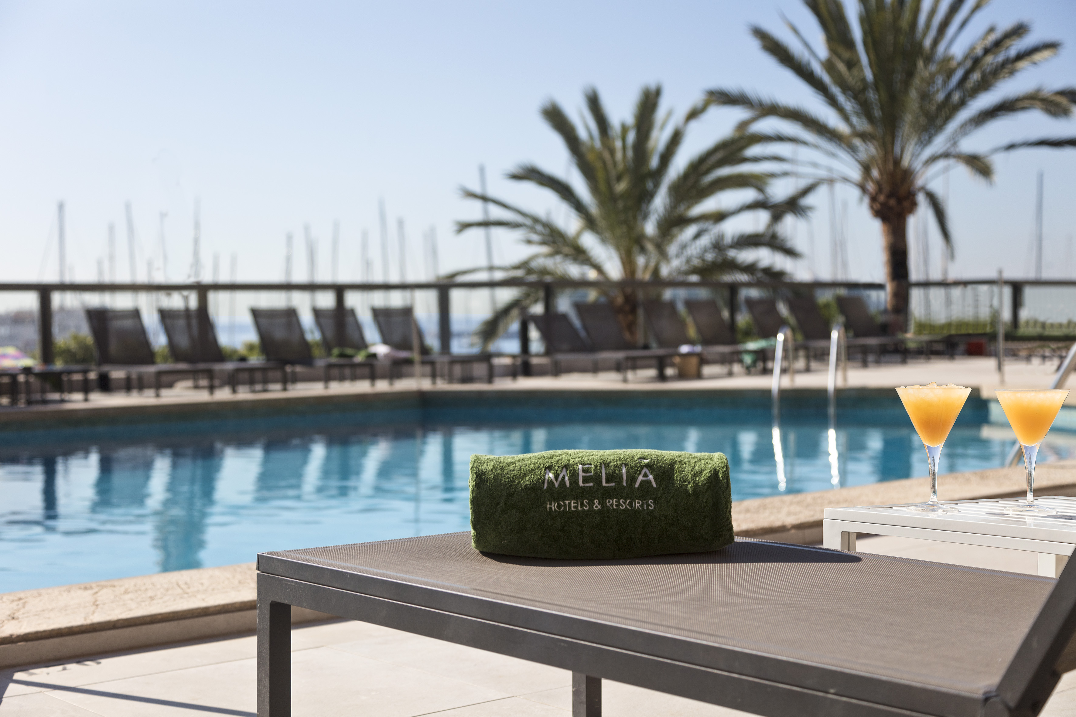 Meliá Hotels & Resorts pool with branded towel, cocktails, lounge chairs, and palm trees.