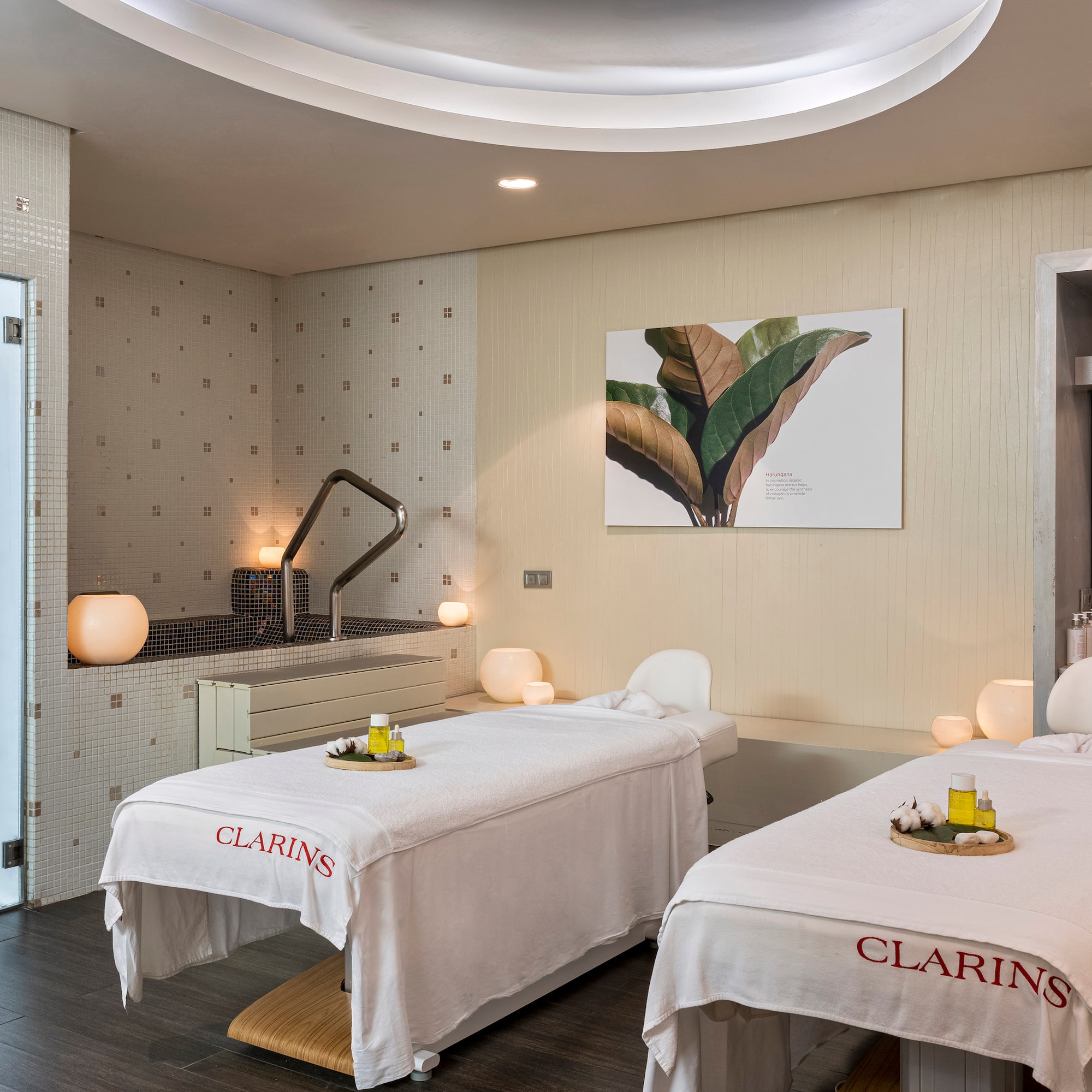 Bright Clarins spa treatment room with two massage beds, tiled pool, and vanity.