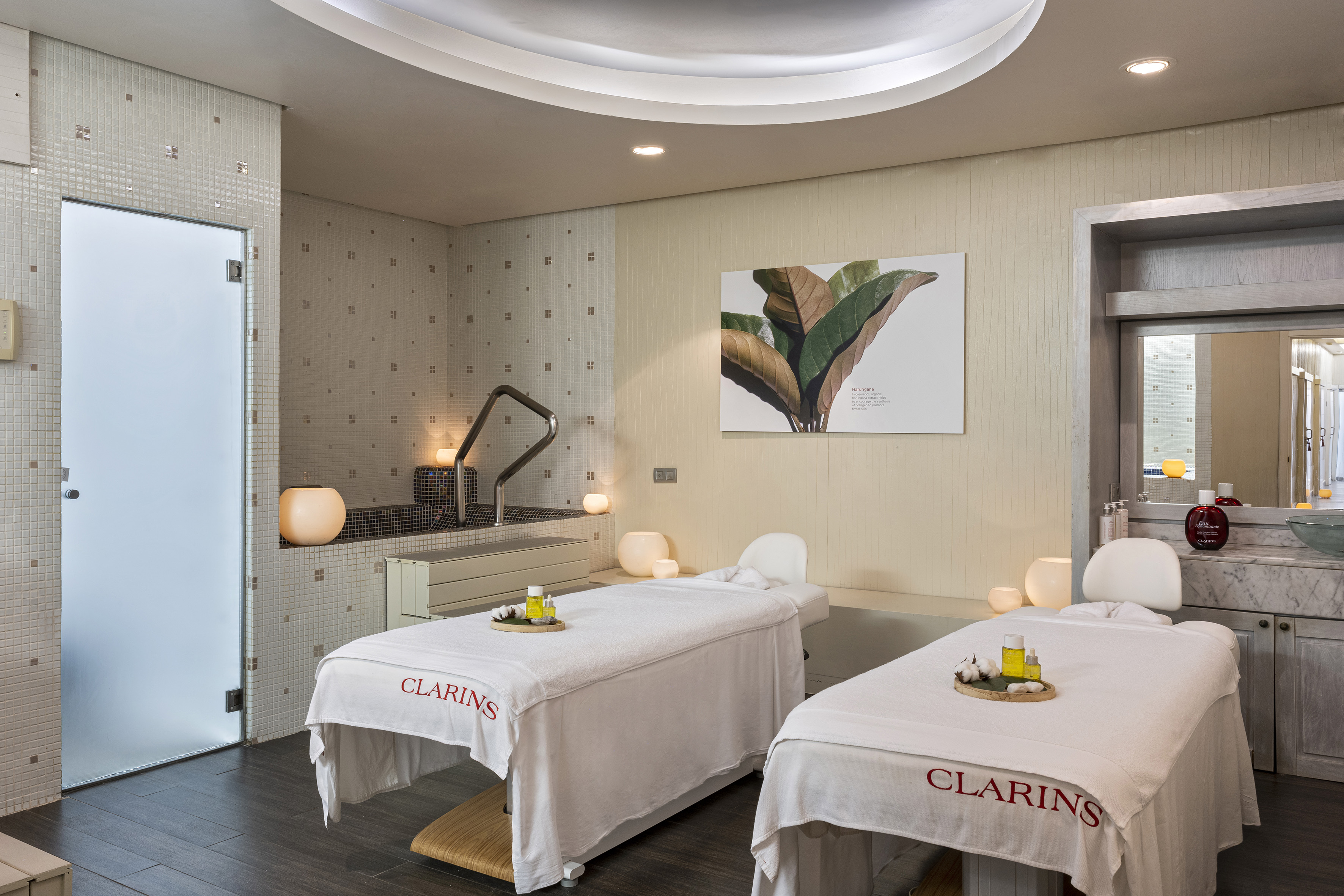 Clarins spa treatment room with two massage beds, hot tub, and tiled walls.
