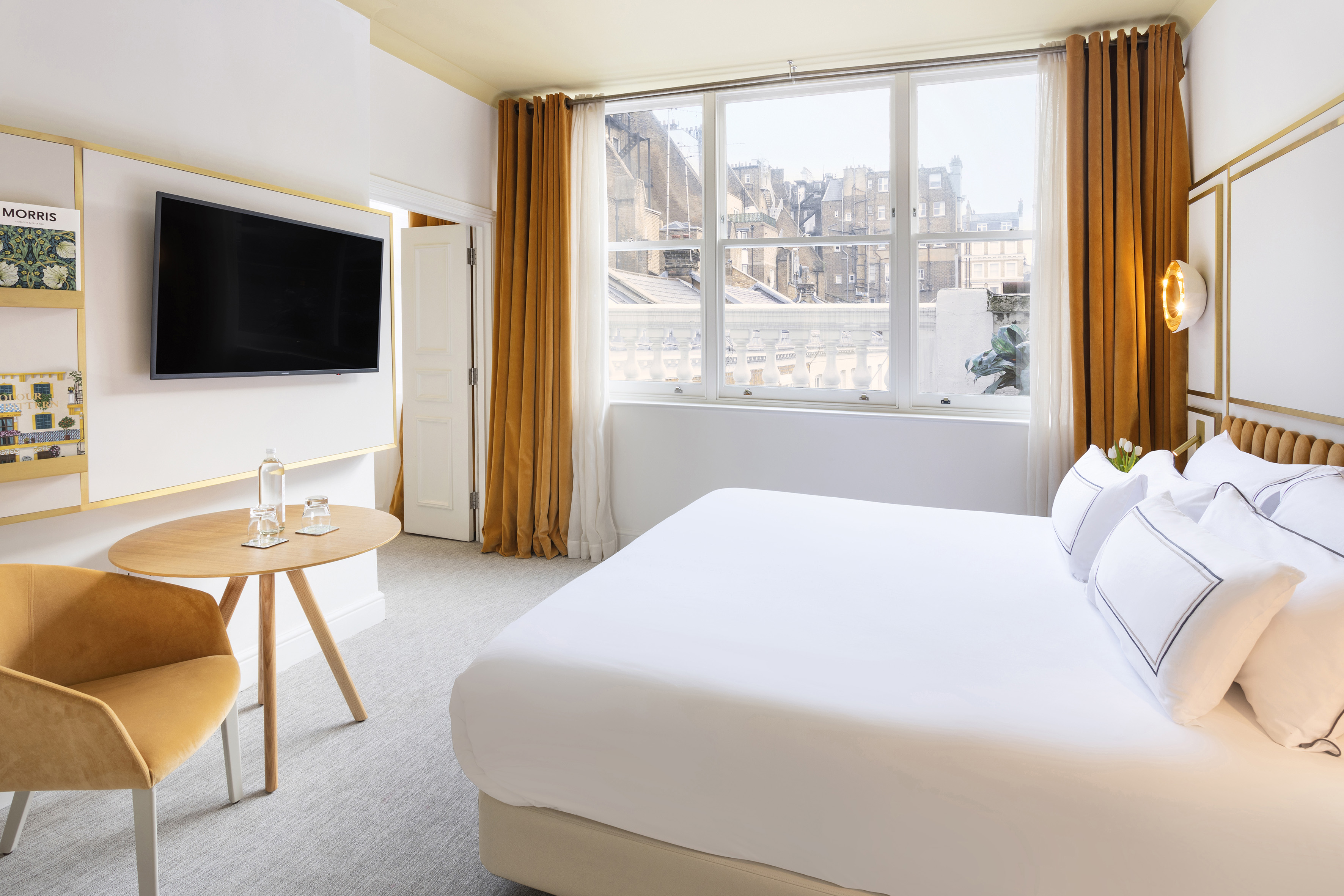 Luxury hotel room with large bed, TV, city view, and golden curtains.