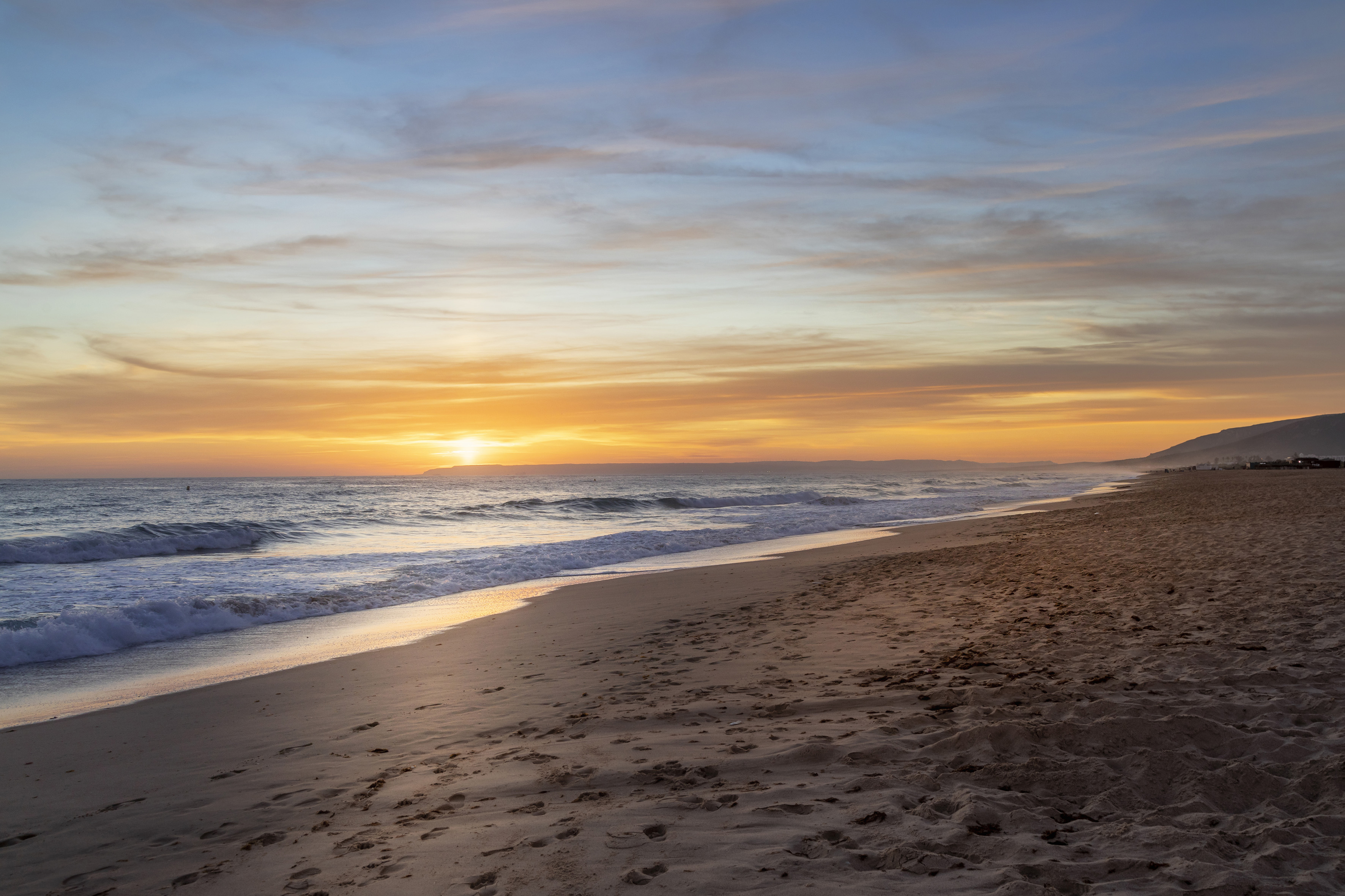 Golden sunset on sandy beach, ocean waves, and vibrant sky.