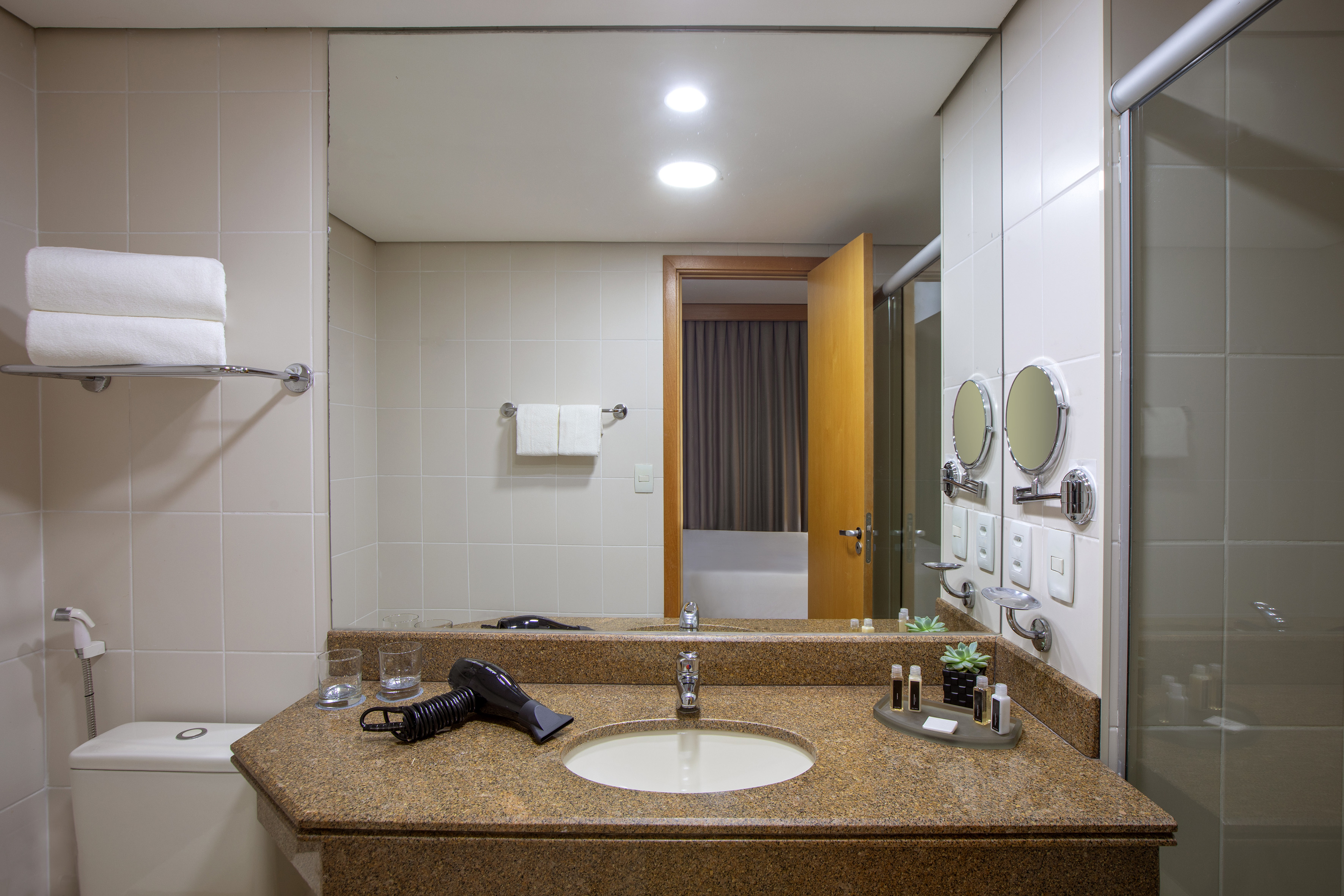 Hotel bathroom vanity with granite countertop, sink, mirror, towels, toiletries.