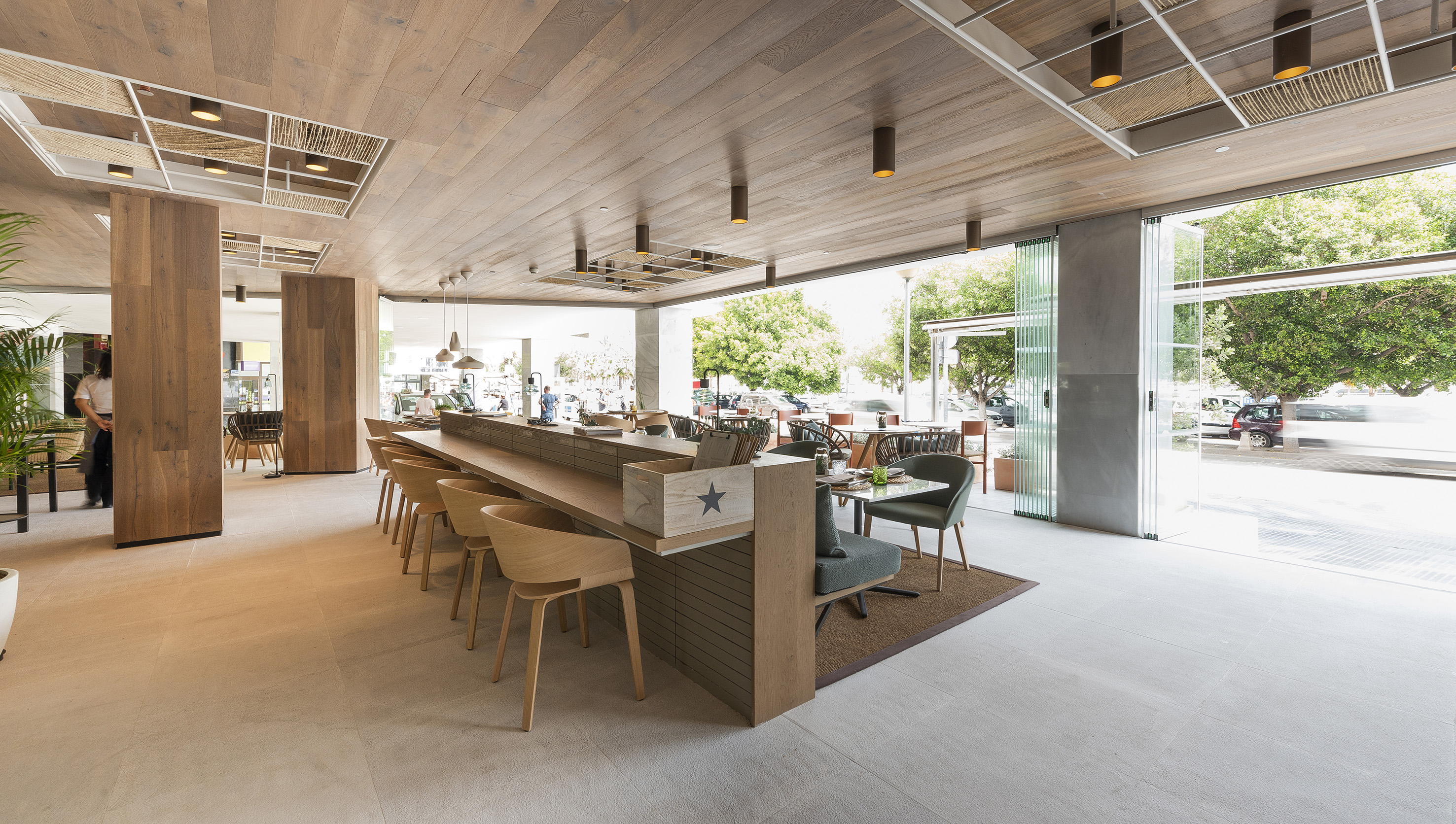 Contemporary wooden restaurant bar with open glass doors and outdoor view.