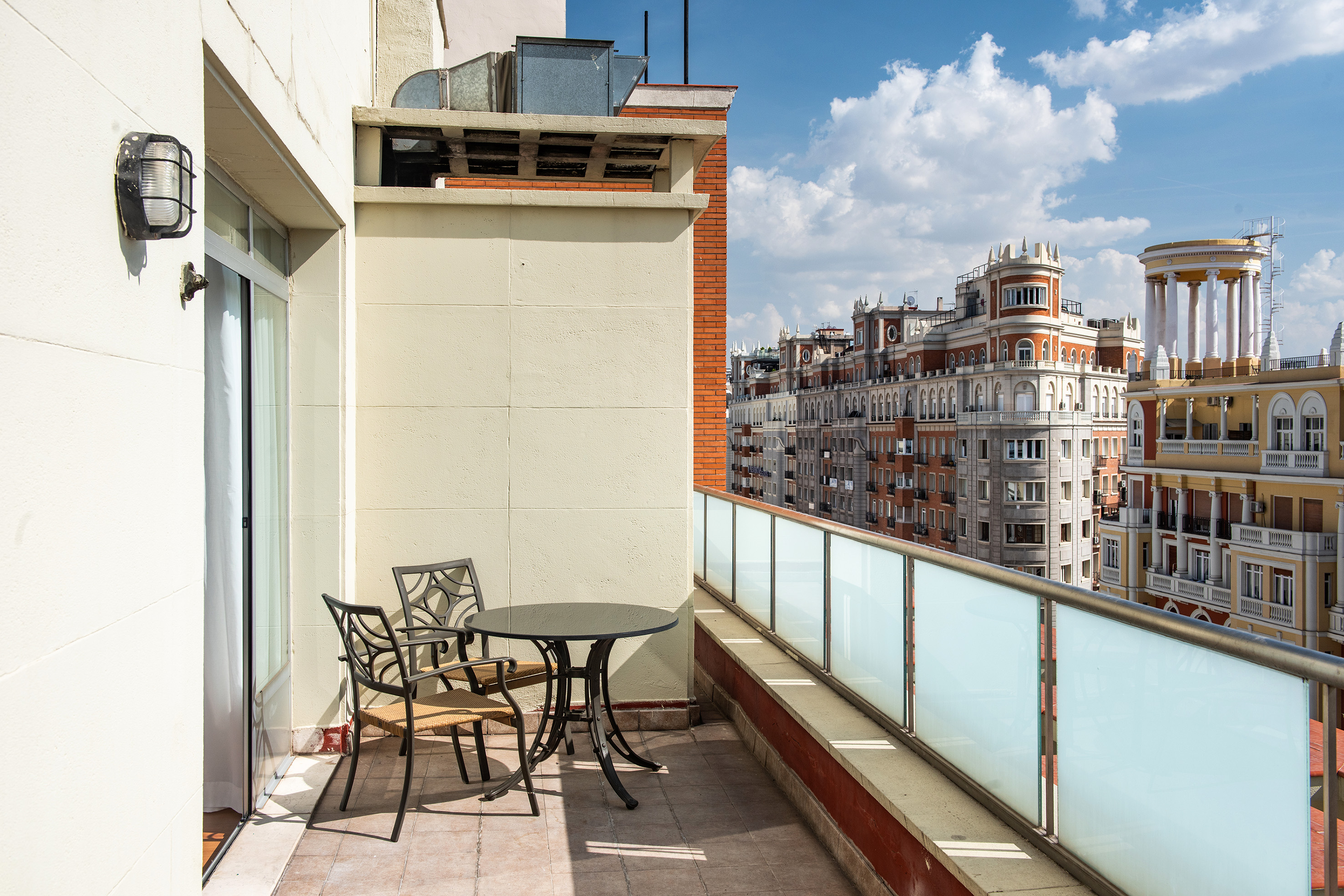 Balcony with outdoor seating, glass railing, and classic Madrid city view.
