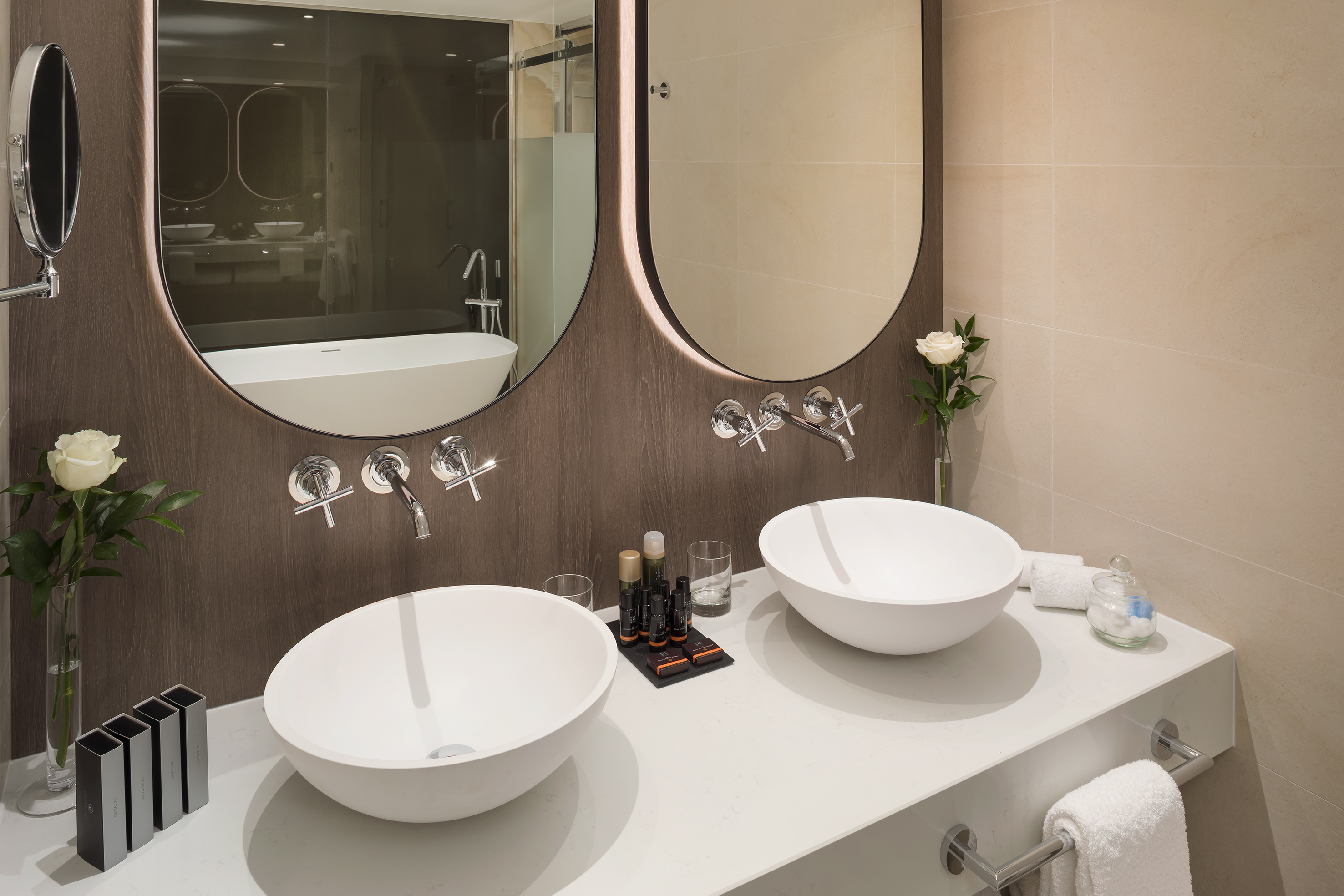 Modern double vanity with white vessel sinks and backlit oval mirrors.